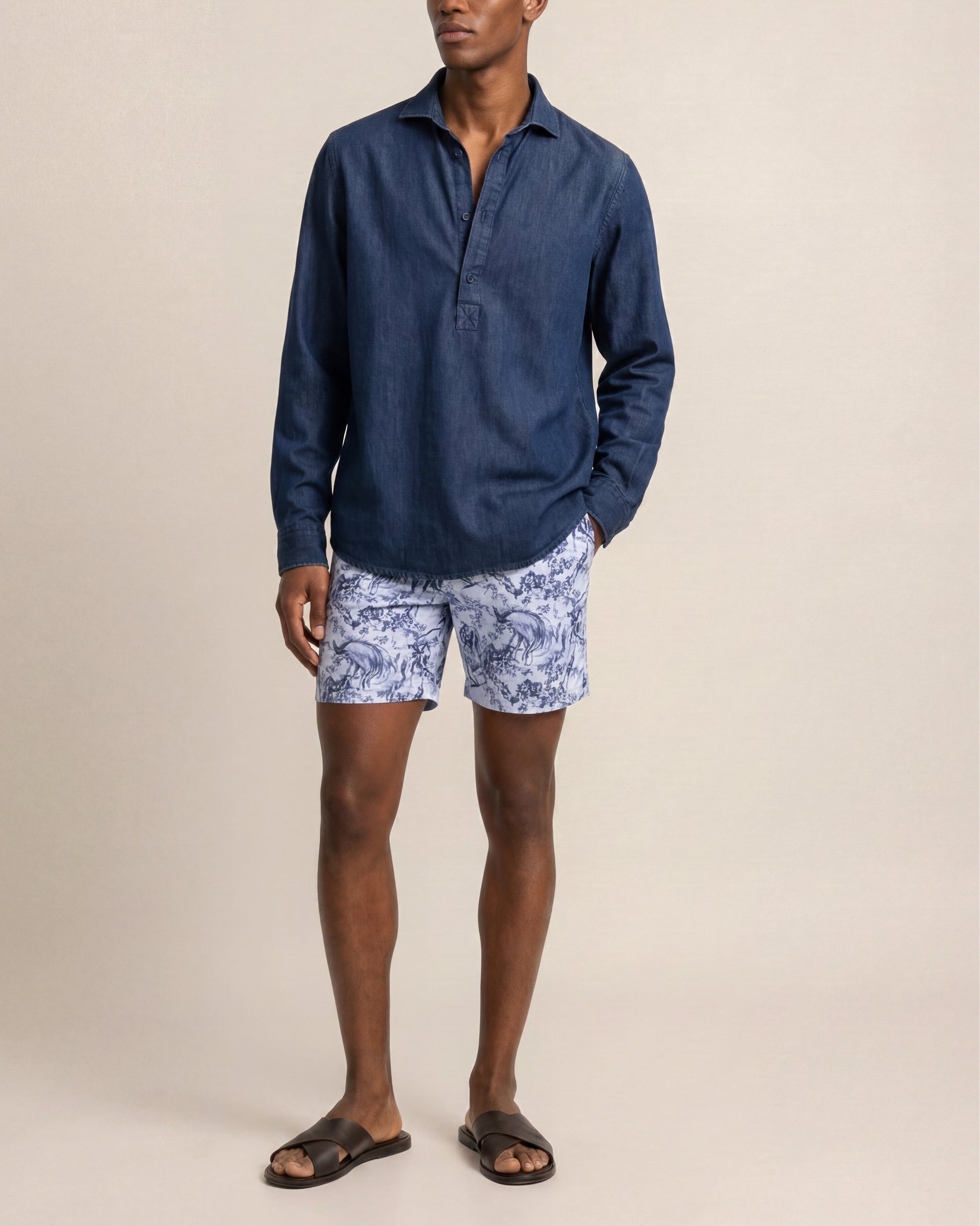 Man wearing a blue long-sleeve shirt and patterned shorts on a beige background