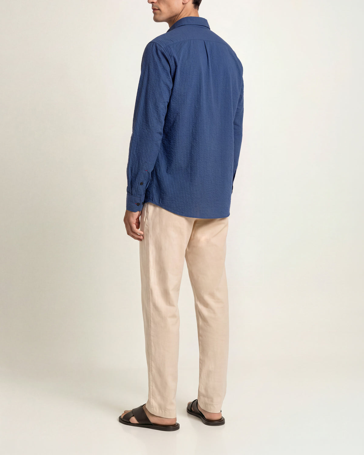 Man wearing dark blue shirt and beige trousers and brow sandals on a plain background