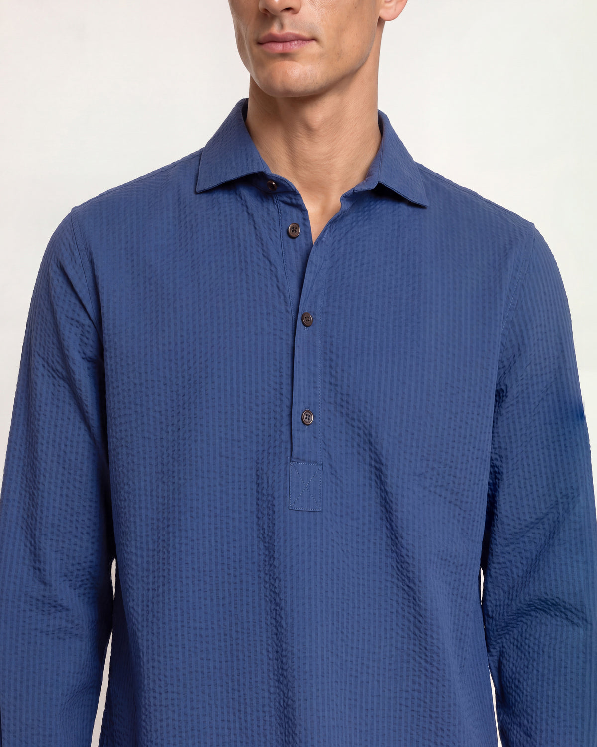Closeup of man wearing dark navy overhead button up shirt on a plain background