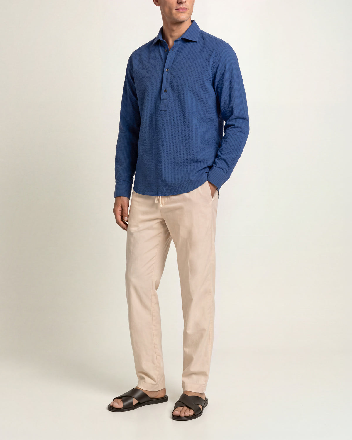 Man wearing dark blue long sleeve overhead shirt with beige trousers on a plain background