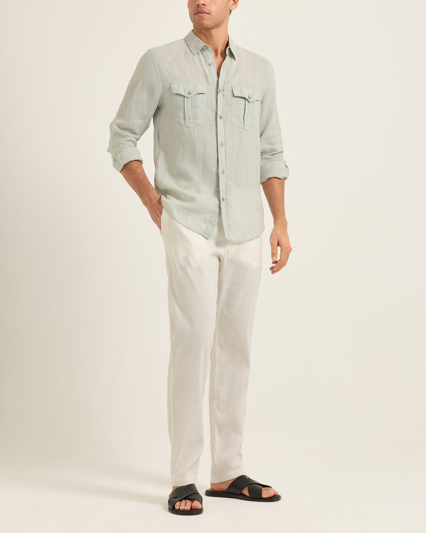 Man wearing a light green button-up shirt and white pants on a plain background