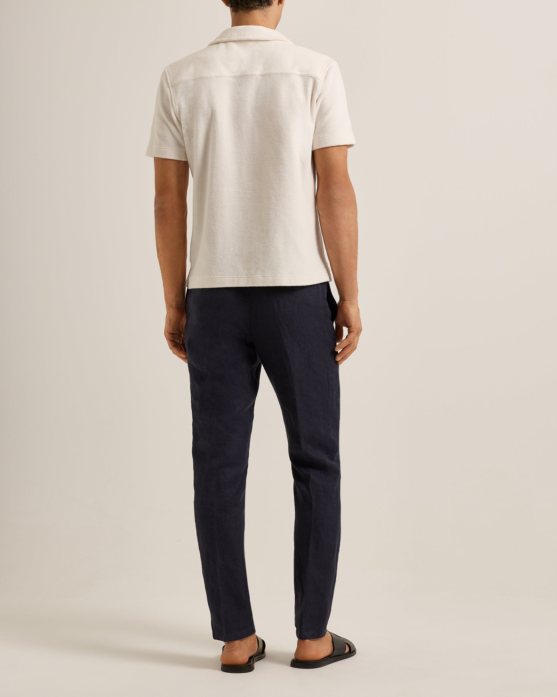 Person wearing a white polo shirt and navy pants on a beige background