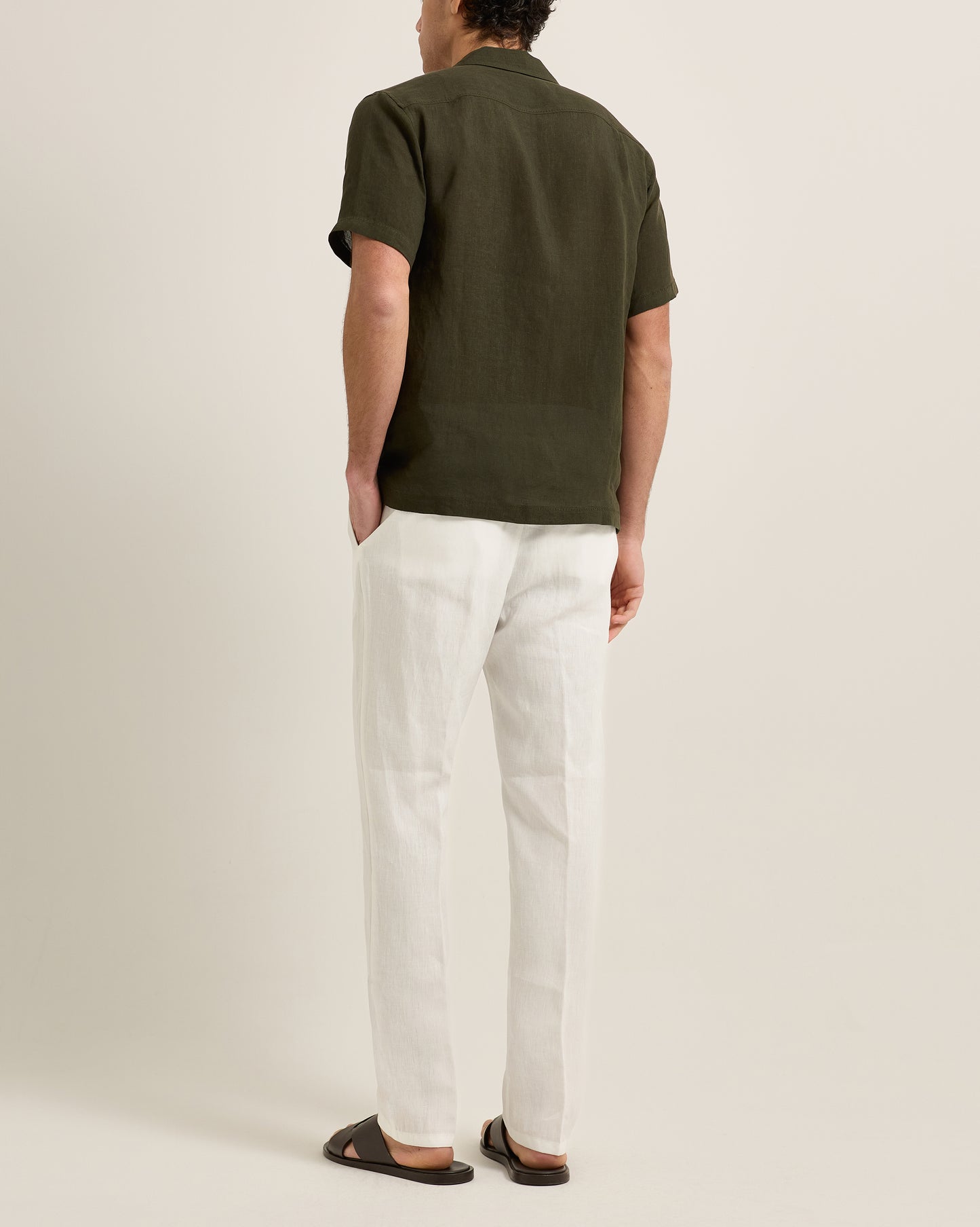 Person wearing a green polo shirt and white pants on a beige background