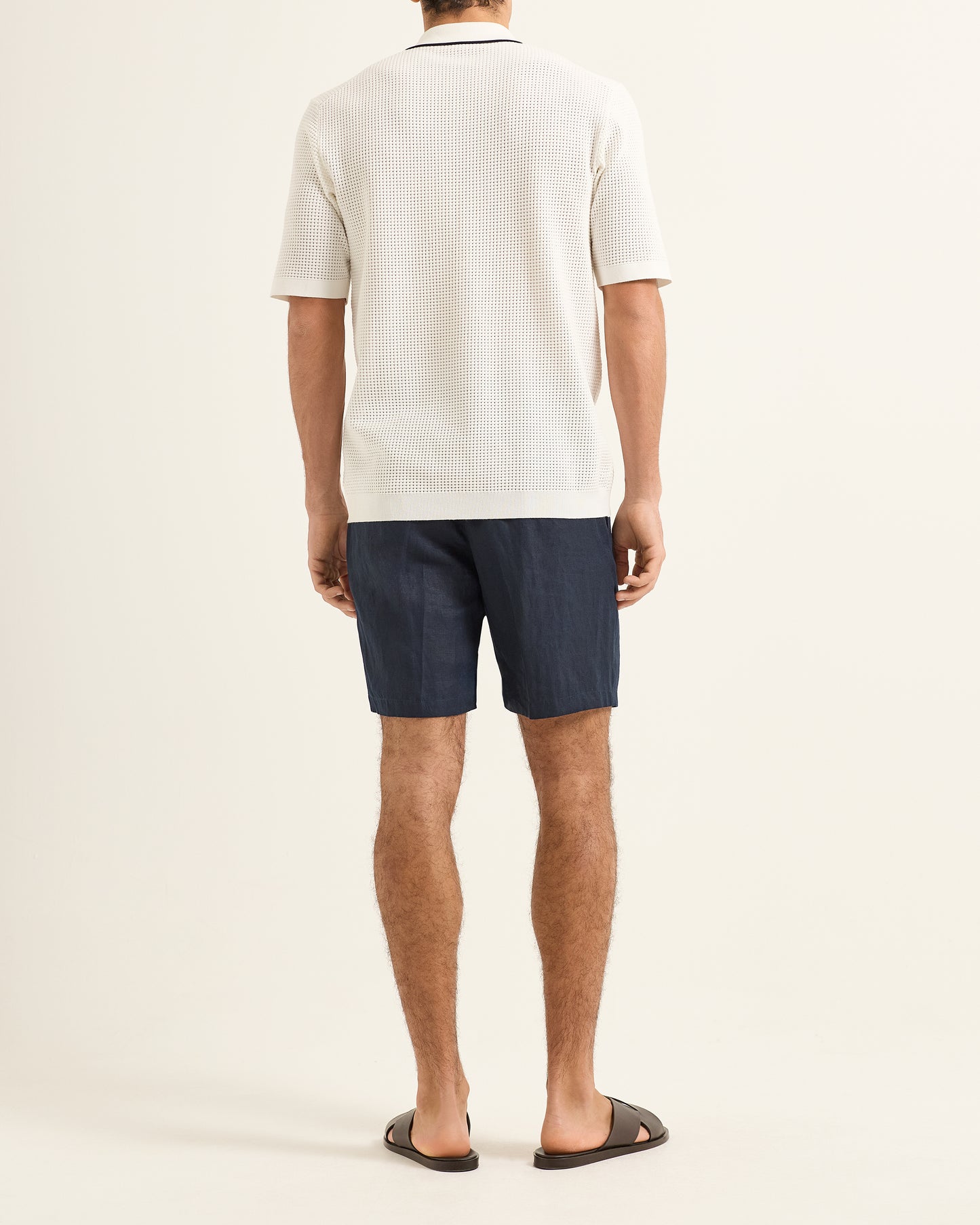 Person wearing a white polo shirt and dark shorts on a plain background