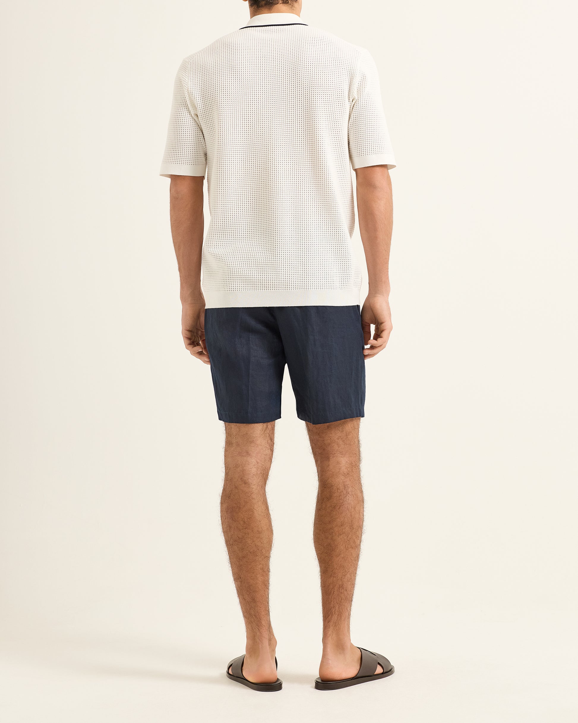 Person wearing a white polo shirt and dark shorts on a plain background