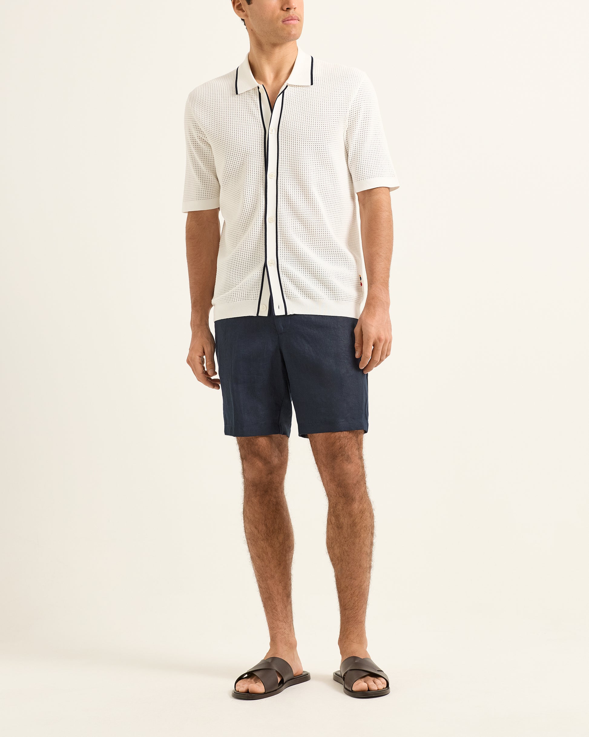 Man wearing a white polo shirt with black trim and navy shorts on a plain background
