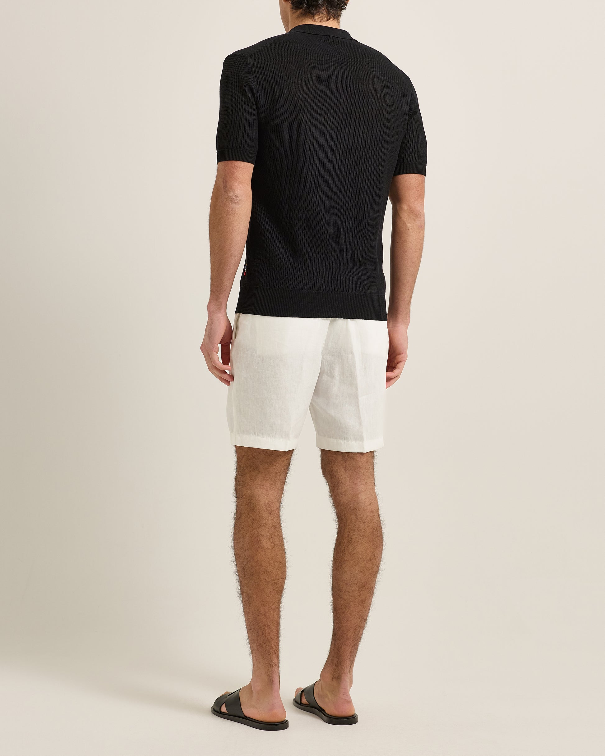 Man wearing a black polo shirt and white shorts on a beige background