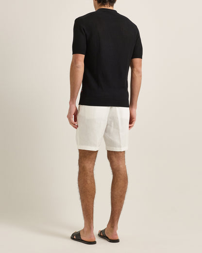 Man wearing a black polo shirt and white shorts on a beige background