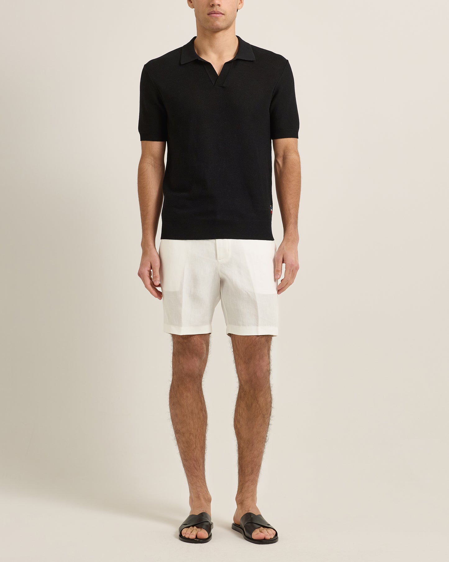 Man wearing a black polo shirt and white shorts on a beige background