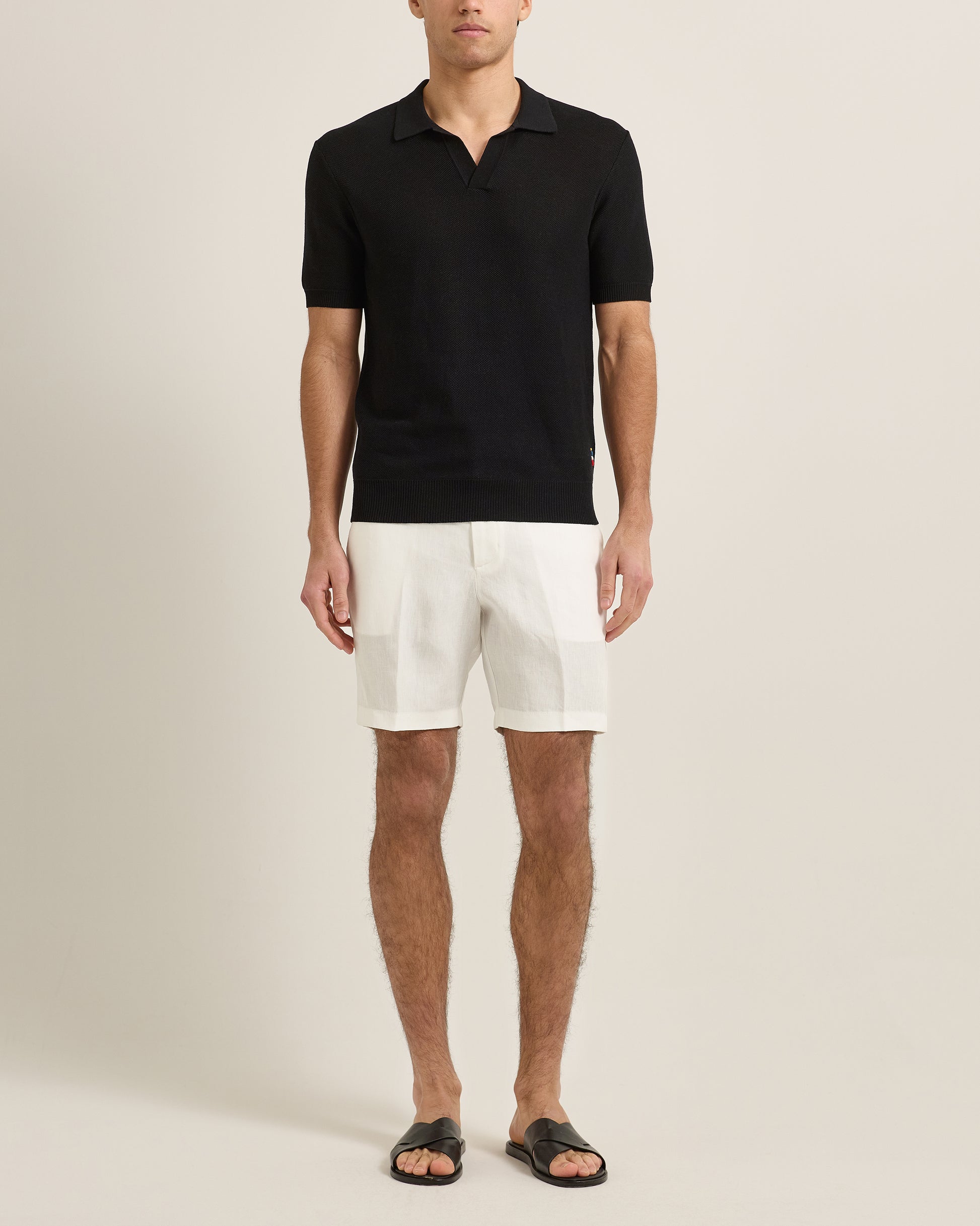 Man wearing a black polo shirt and white shorts on a beige background