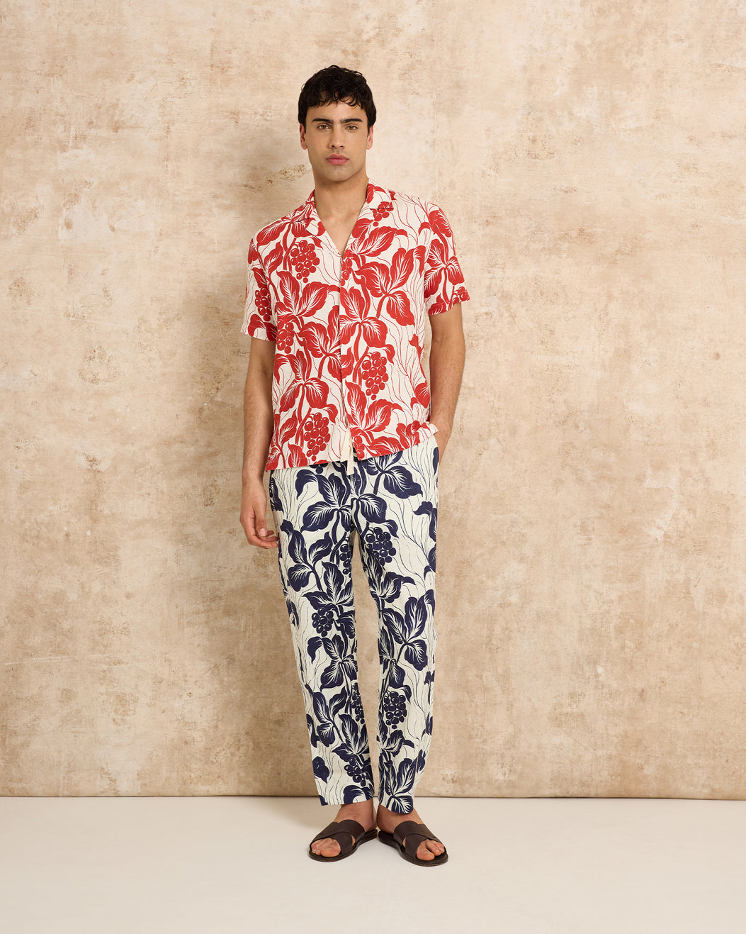 Man wearing red floral shirt with navy floral trousers on a plain background