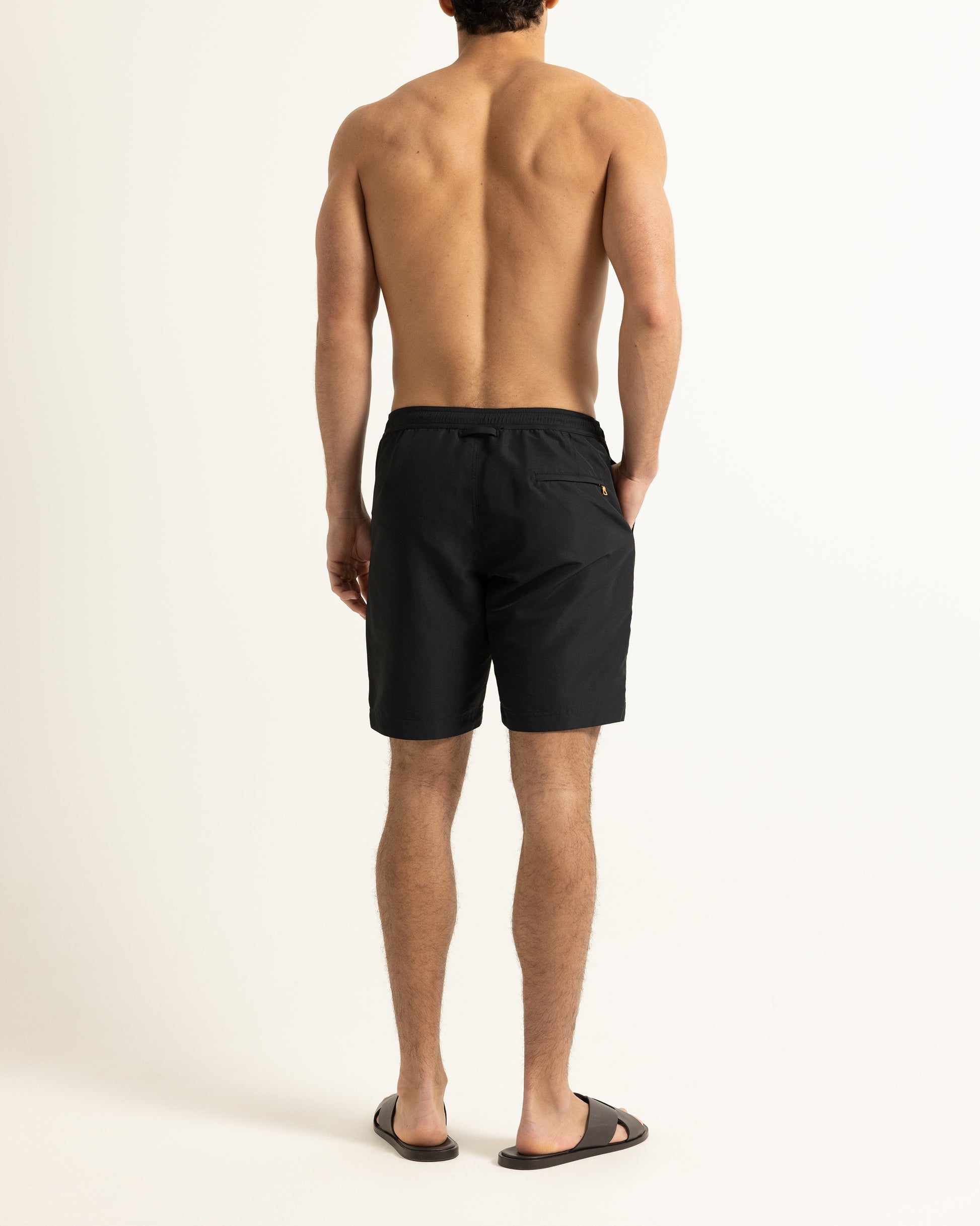 Man wearing black drawstring swim shorts on a plain background