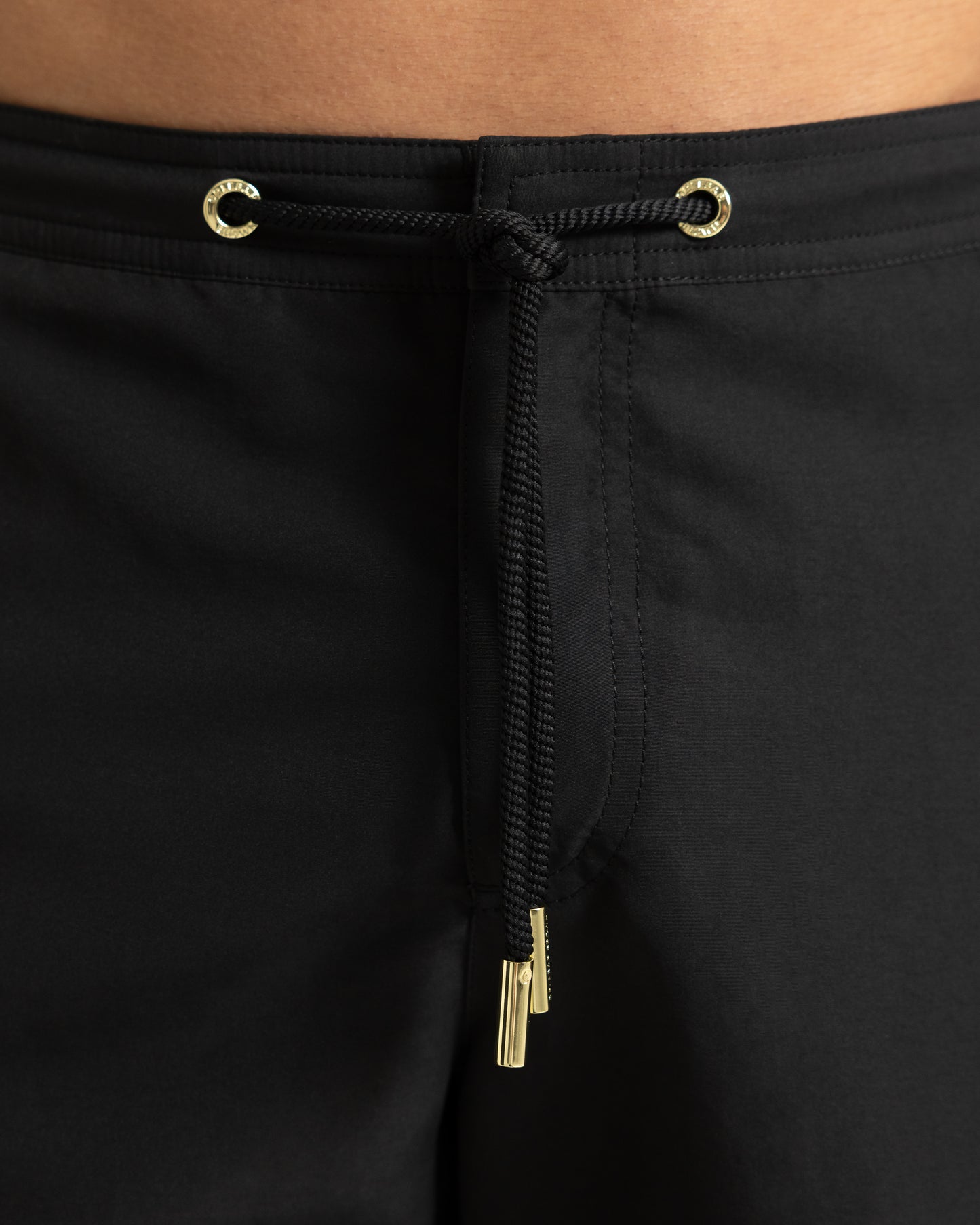Closeup of black drawstring swim shorts with gold eyelet detail