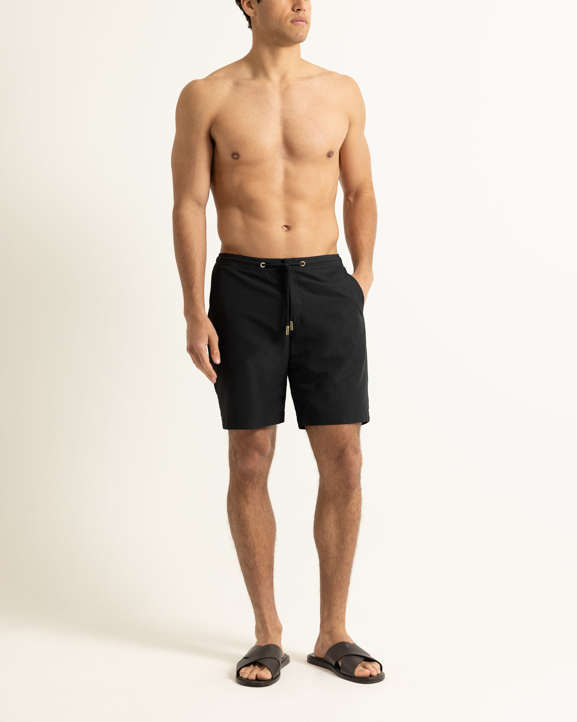 Man wearing black drawstring swim shorts on a plain background