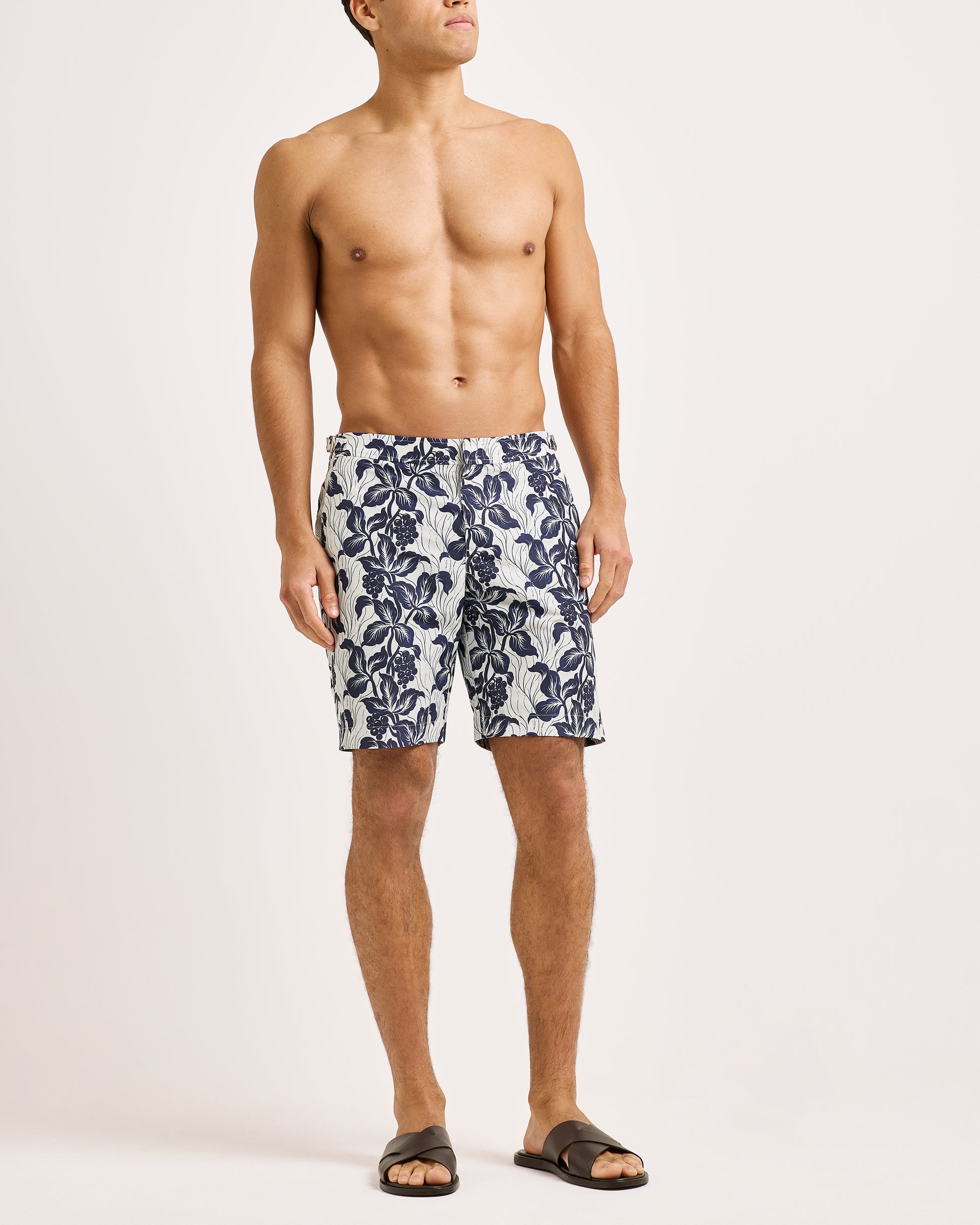 Man wearing navy floral swim shorts on a light pink background