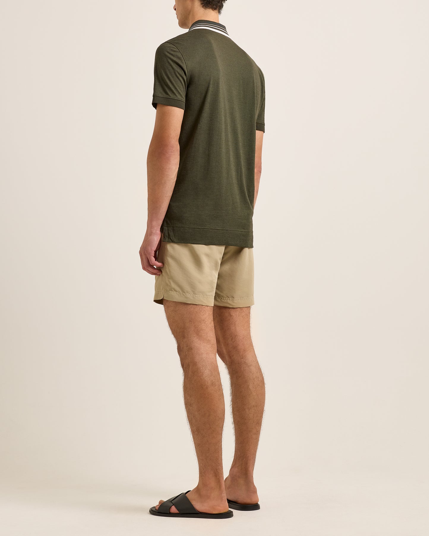 Man wearing a green polo shirt and beige shorts on a plain background