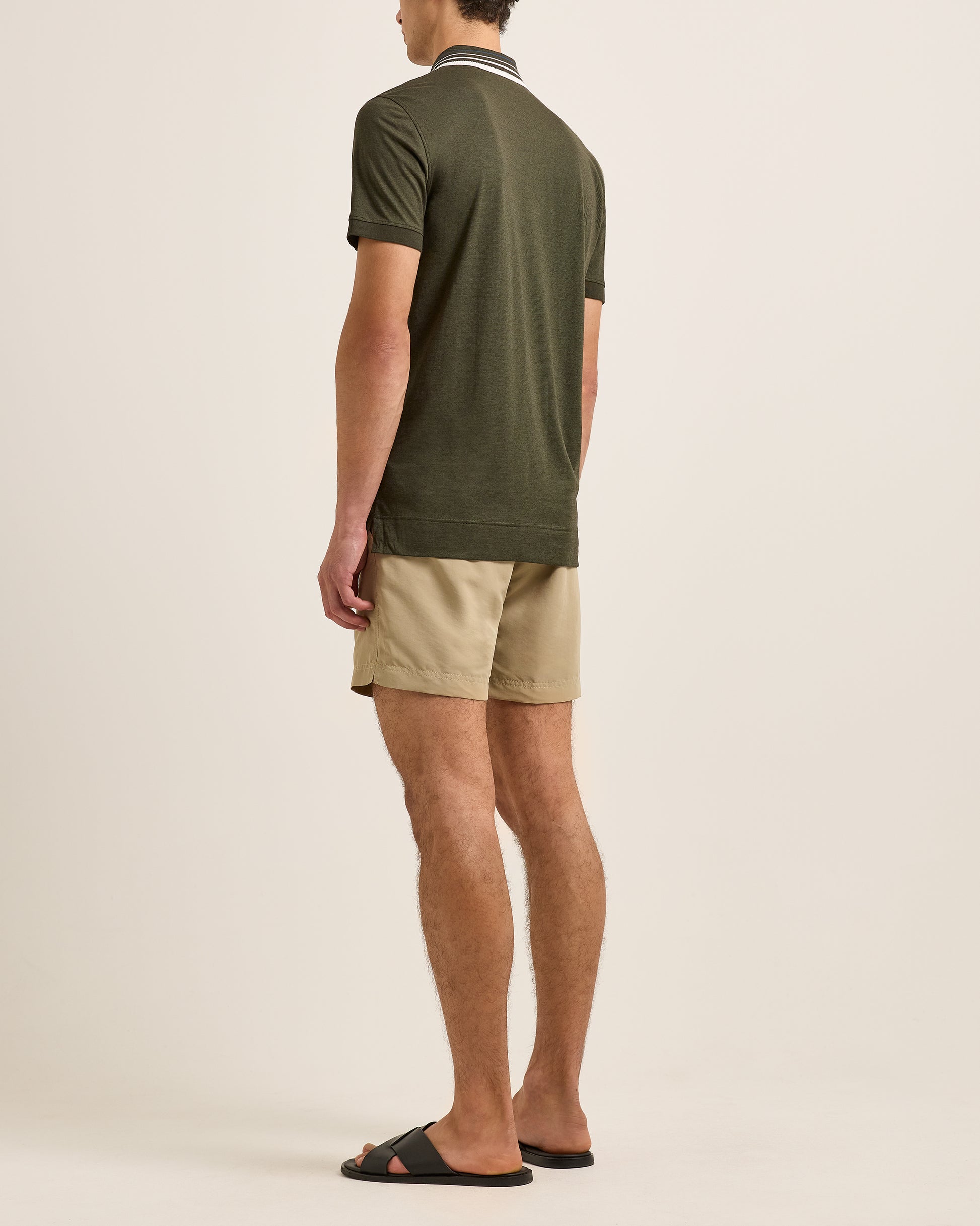 Man wearing a green polo shirt and beige shorts on a plain background