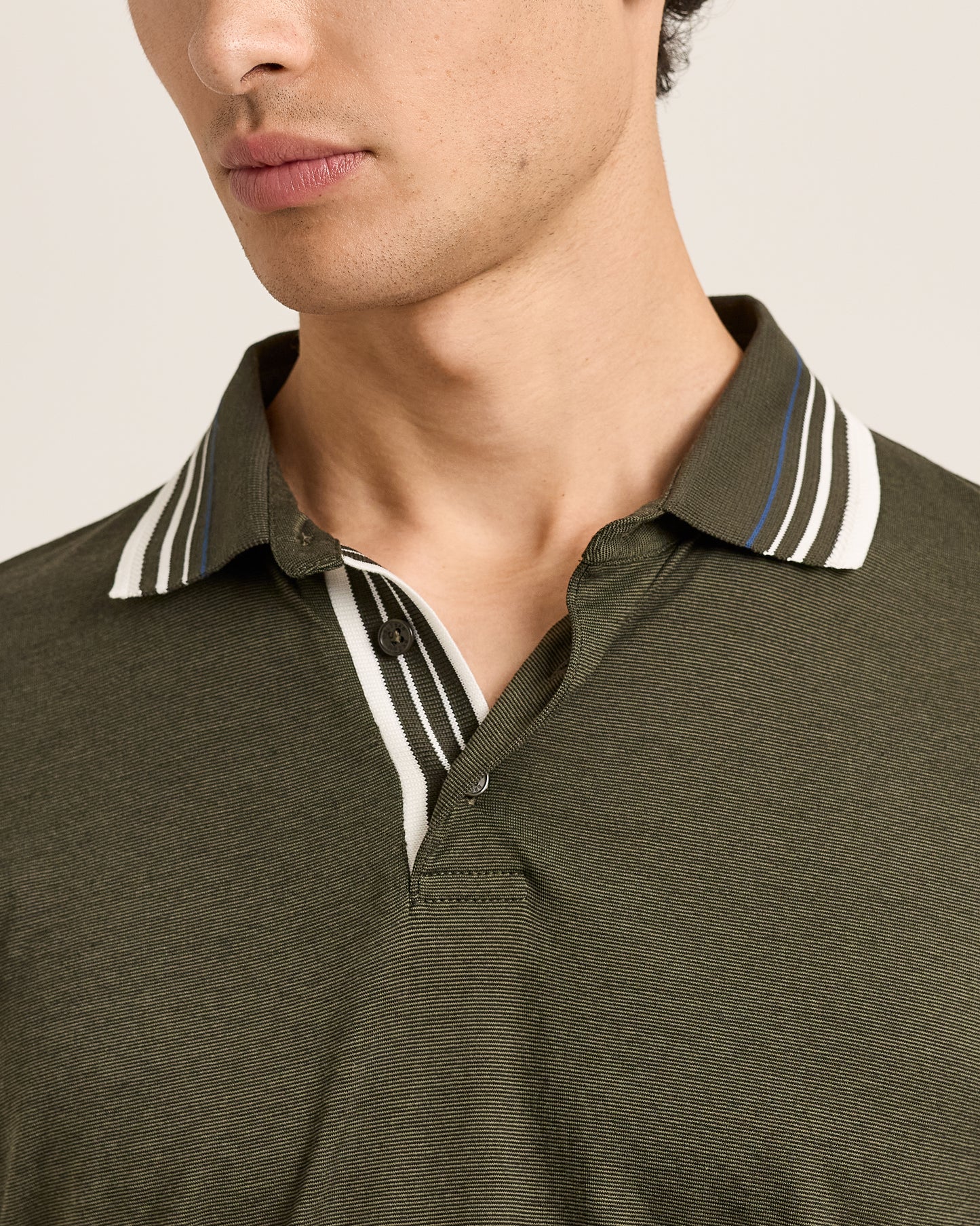Close-up of a man wearing an olive green polo shirt with a striped collar.
