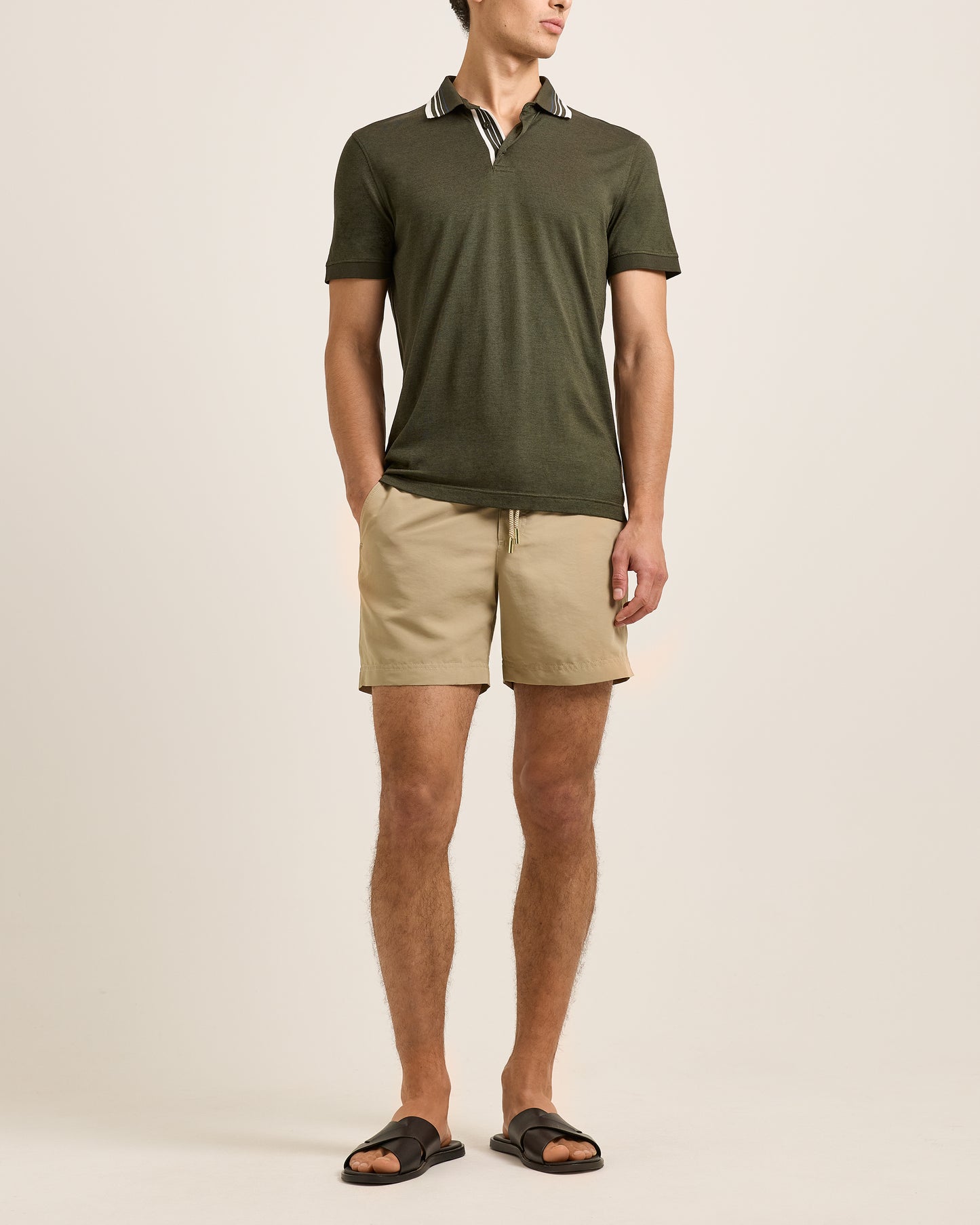 Man wearing a green polo shirt and beige shorts on a plain background
