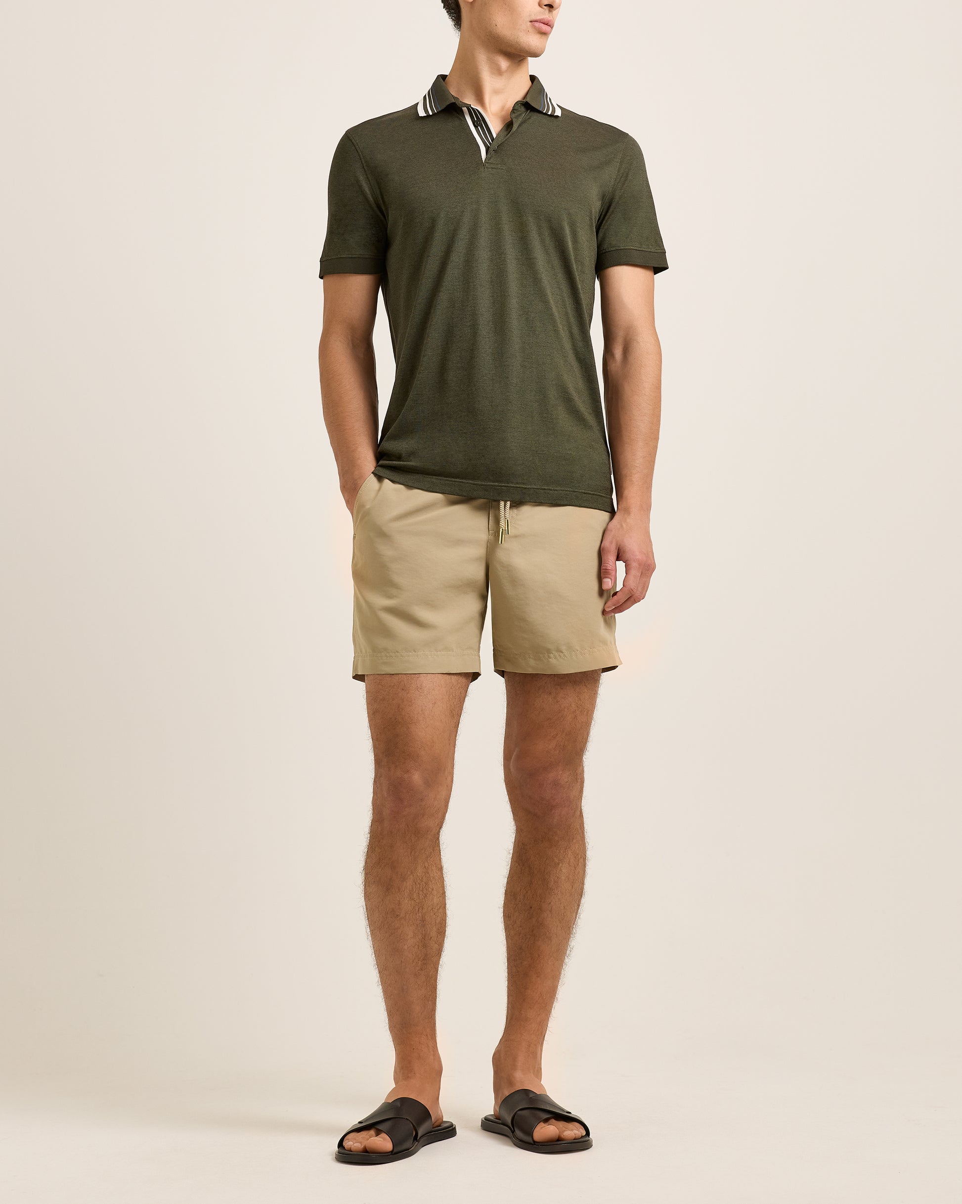 Man wearing a green polo shirt and beige shorts on a plain background