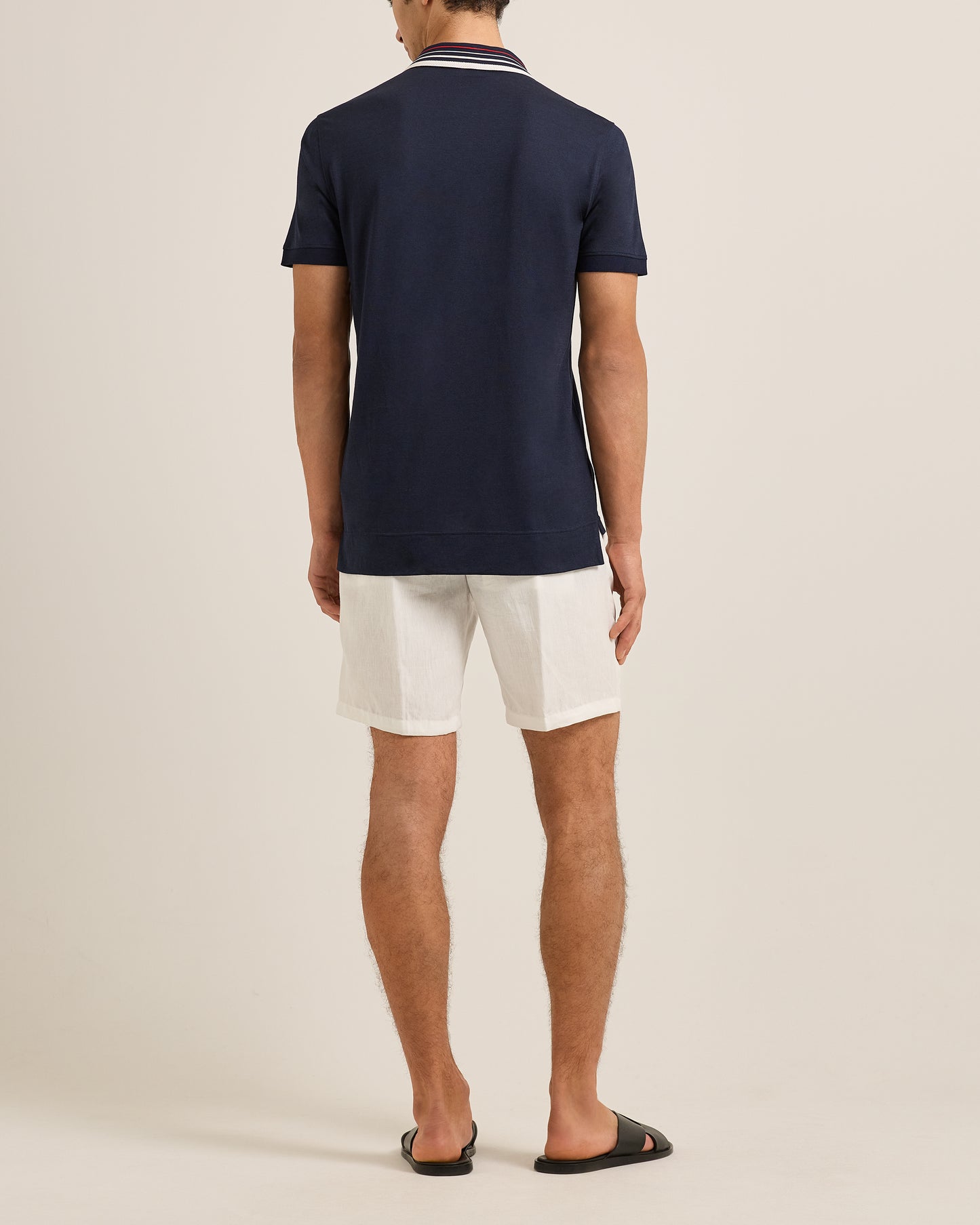 Person wearing a navy polo shirt and white shorts on a beige background