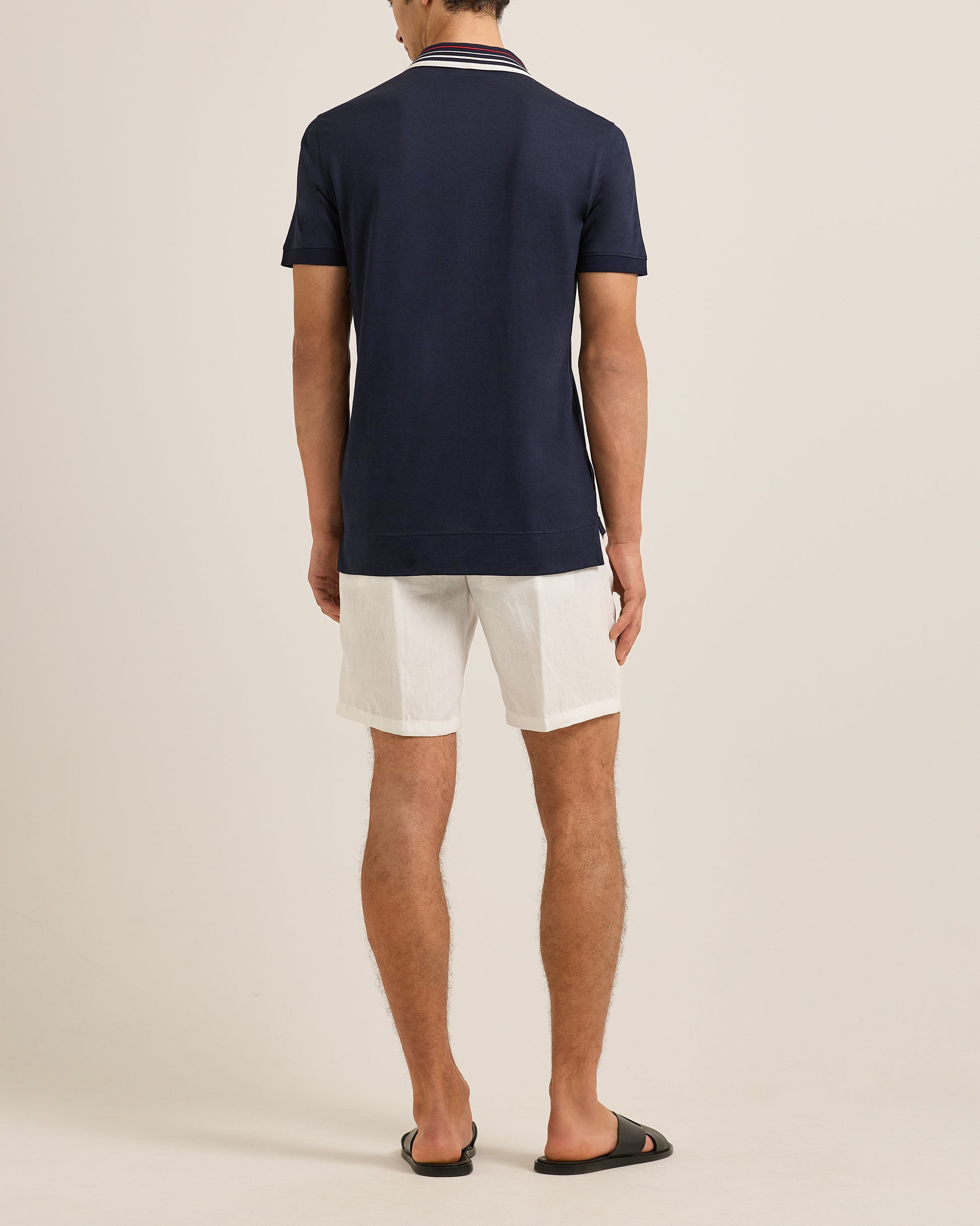Person wearing a navy polo shirt and white shorts on a beige background