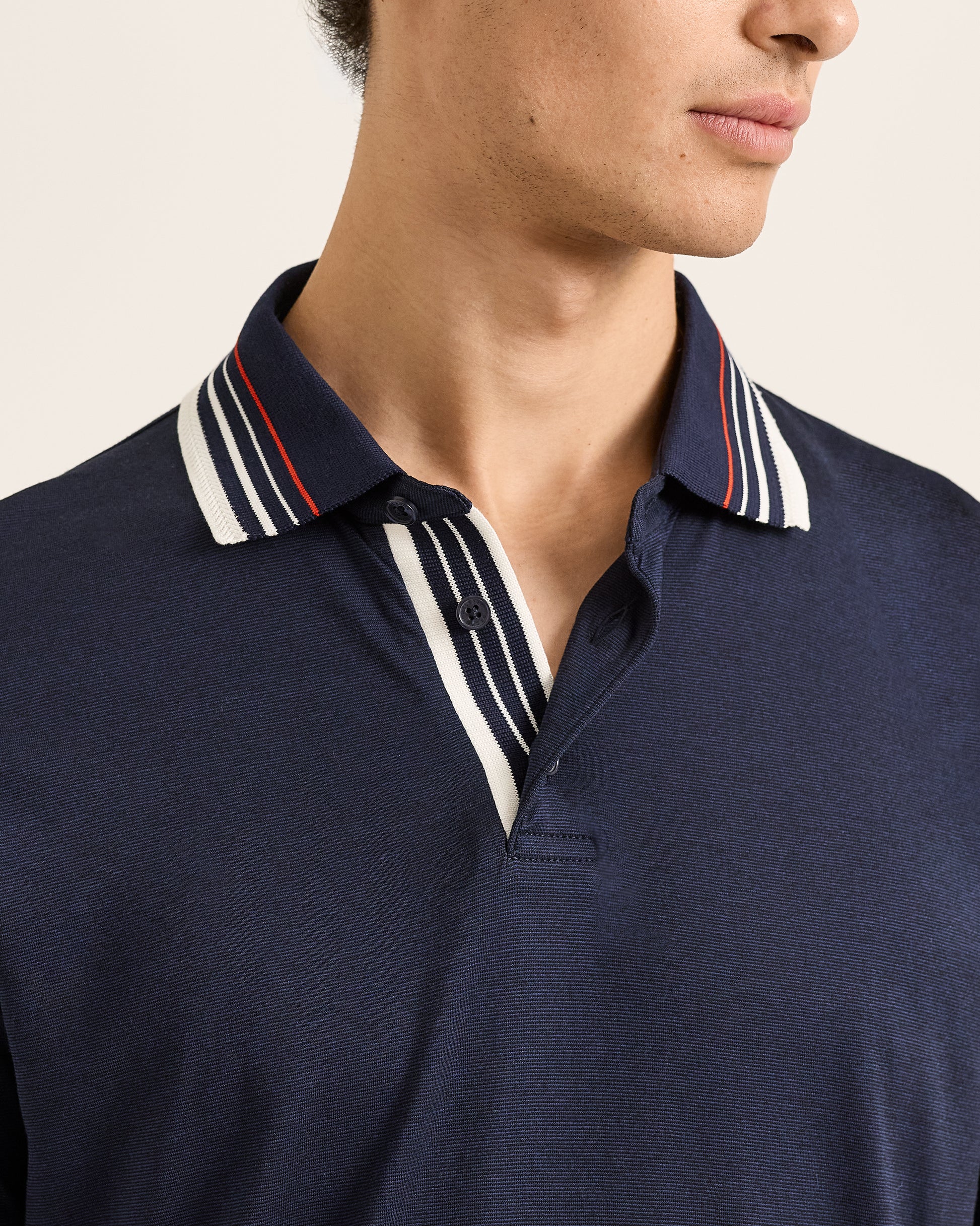 Navy polo shirt with striped collar detail on a neutral background