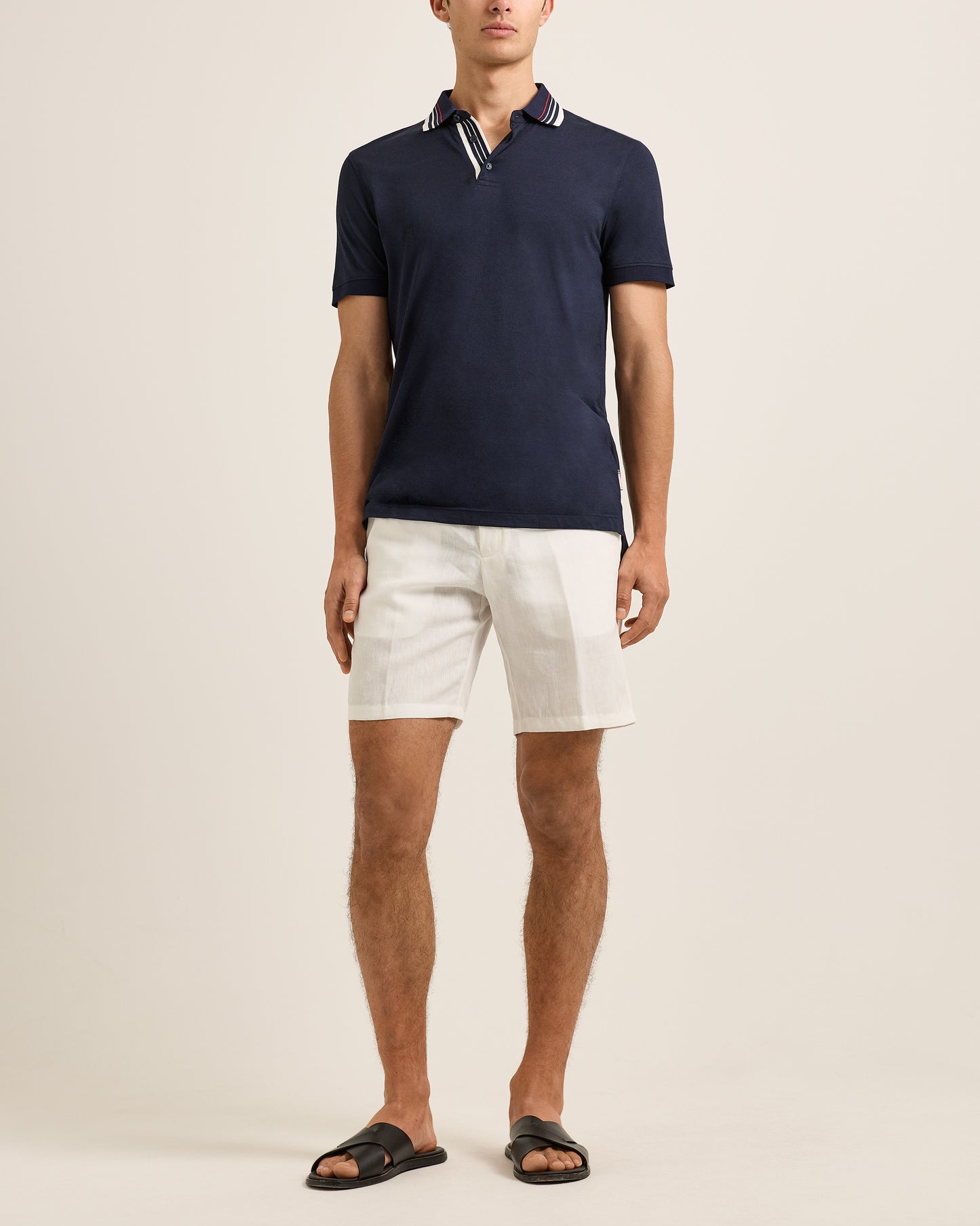 Man wearing a navy polo shirt and white shorts on a beige background