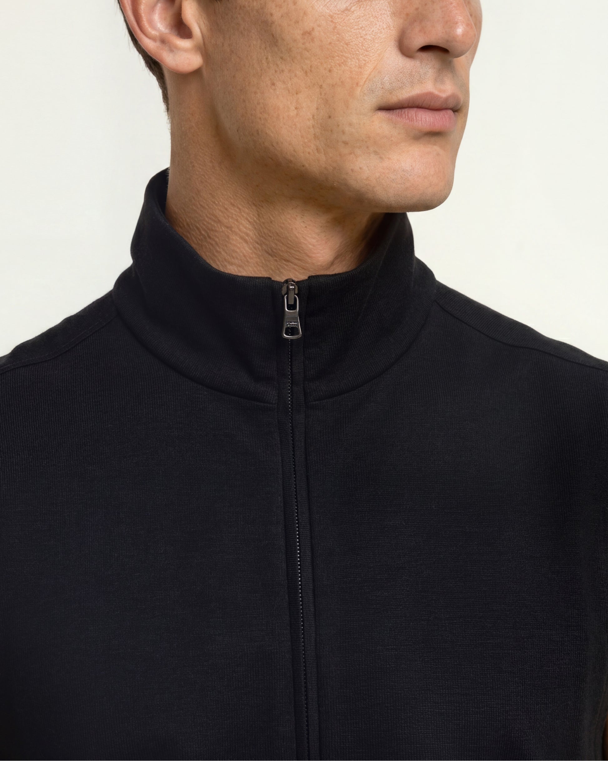 Close-up of a man wearing a black quarter-zip fleece jacket with a stand-up collar, shown from the chest up against a plain light background.