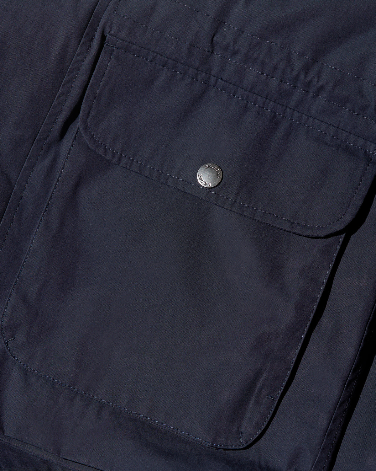 Close-up of a dark navy blue jacket or overshirt showing a large front flap pocket with a single silver metal snap button.