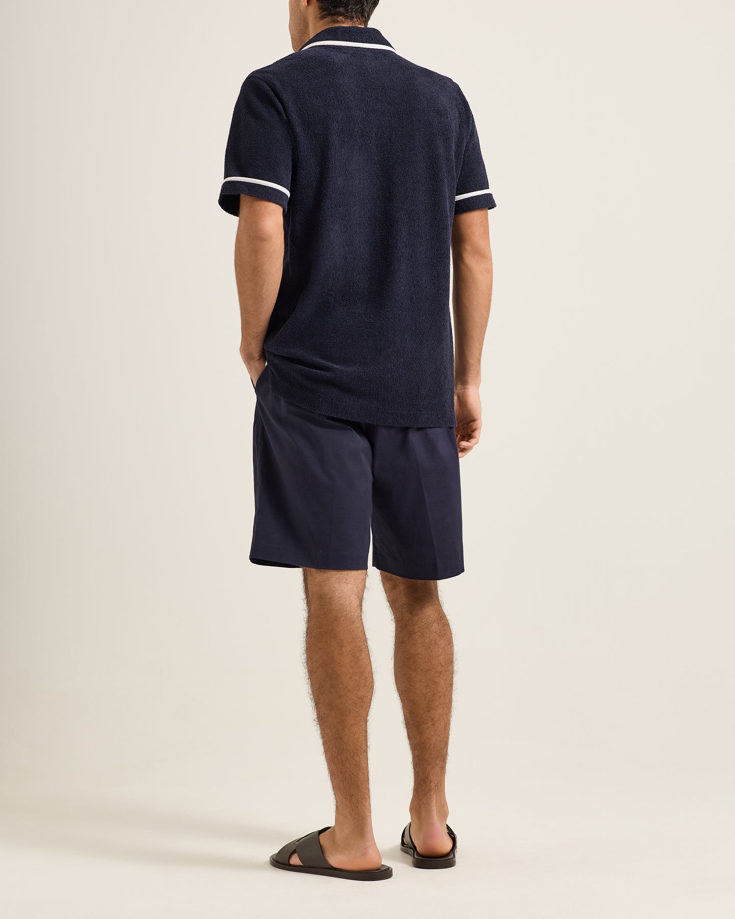 Person wearing a navy blue polo shirt and shorts set on a beige background