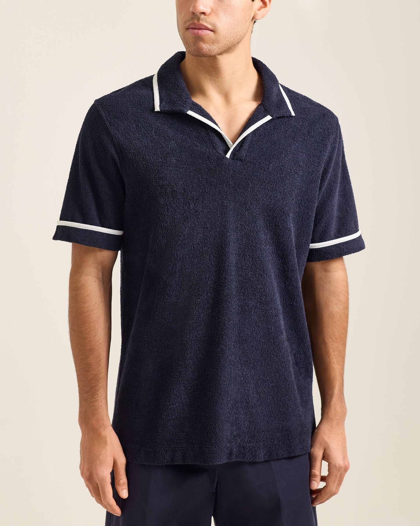 Man wearing a navy polo shirt with white trim on a beige background