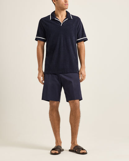 Man wearing a navy blue polo shirt and shorts set on a beige background