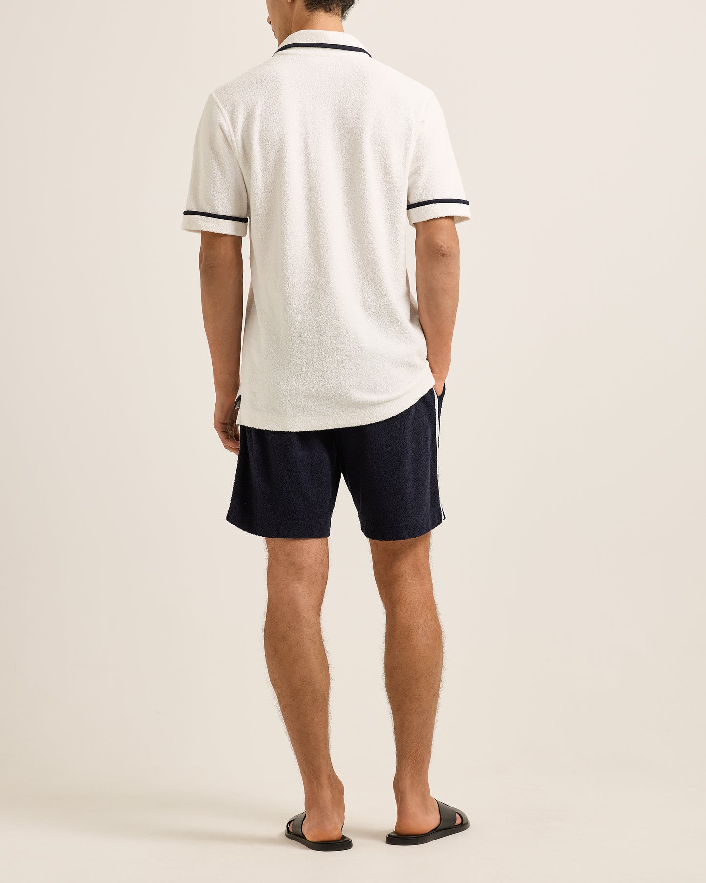 Person wearing a white polo shirt and navy shorts on a plain background