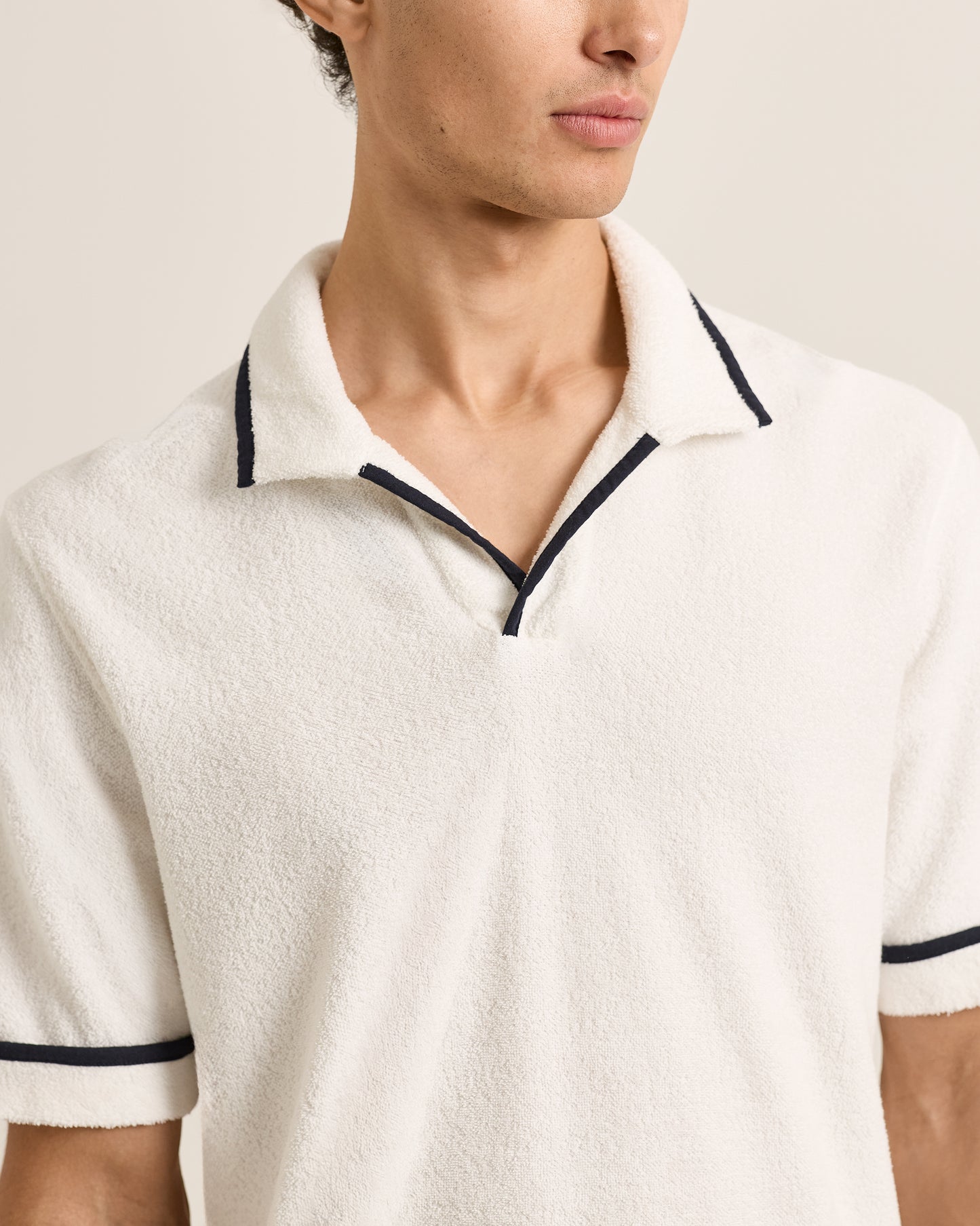 White polo shirt with black trim worn by a person on a neutral background
