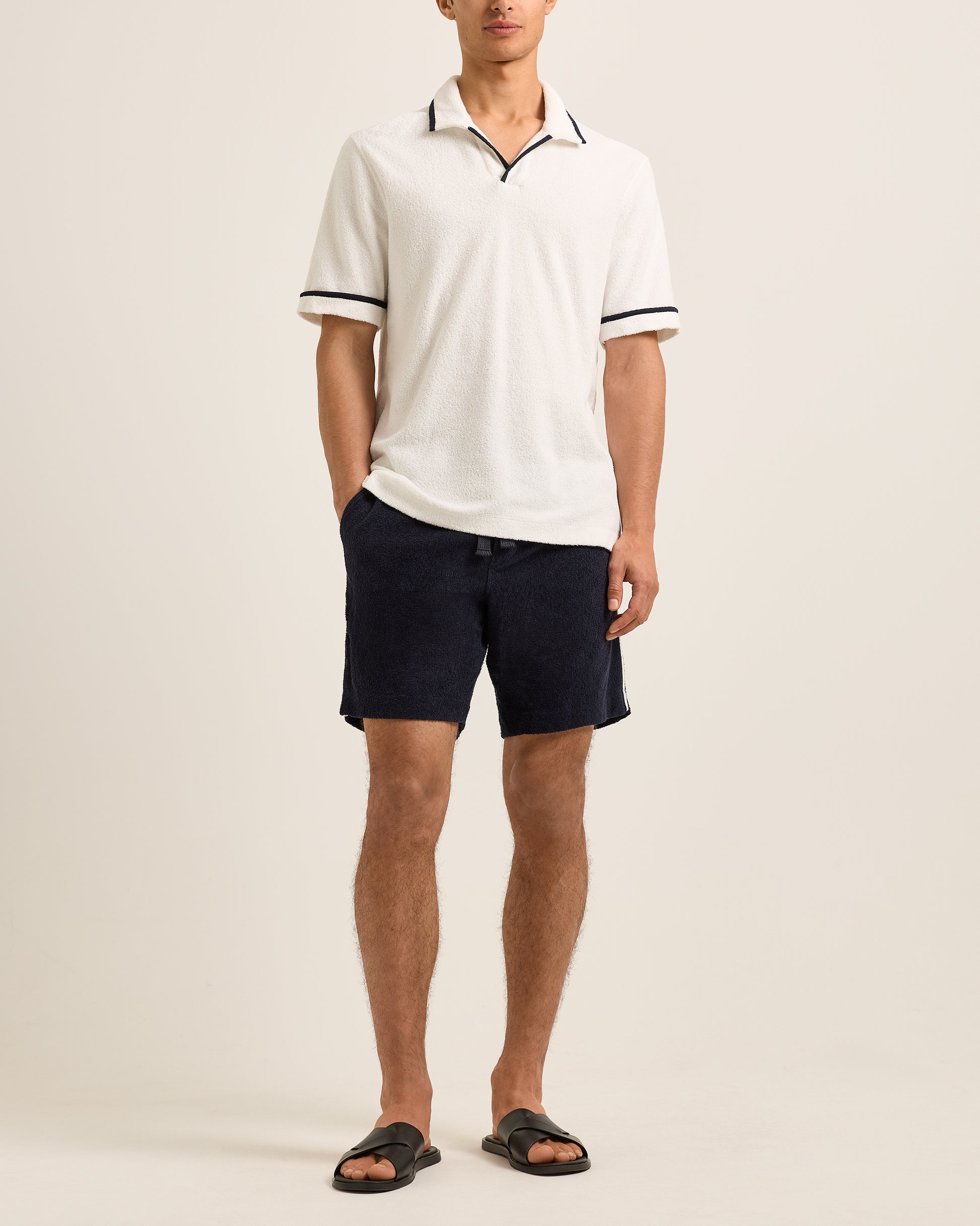 Person wearing a white polo shirt with black trim and navy shorts on a beige background