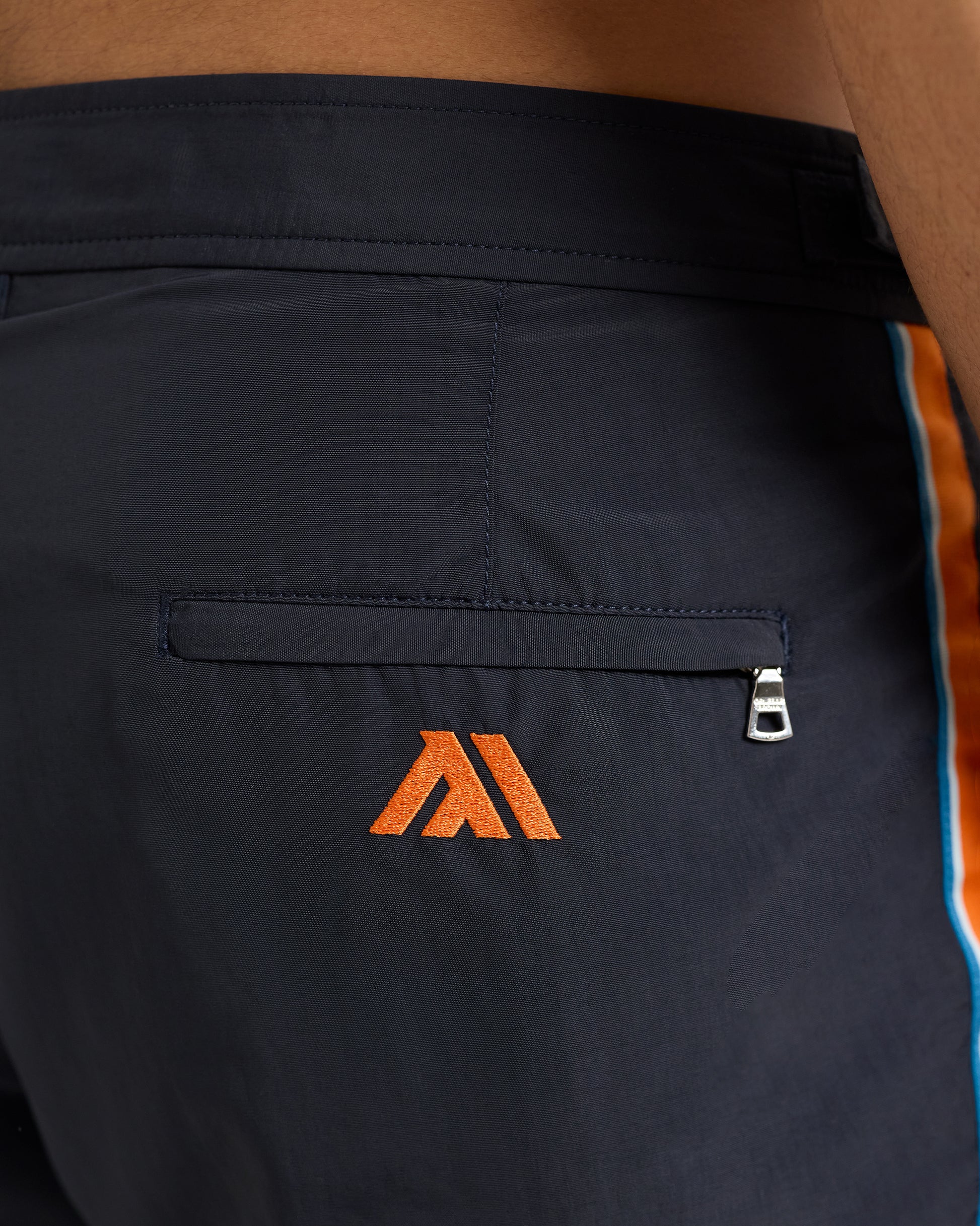 Navy shorts with orange logo on a person wearing a brown shirt.