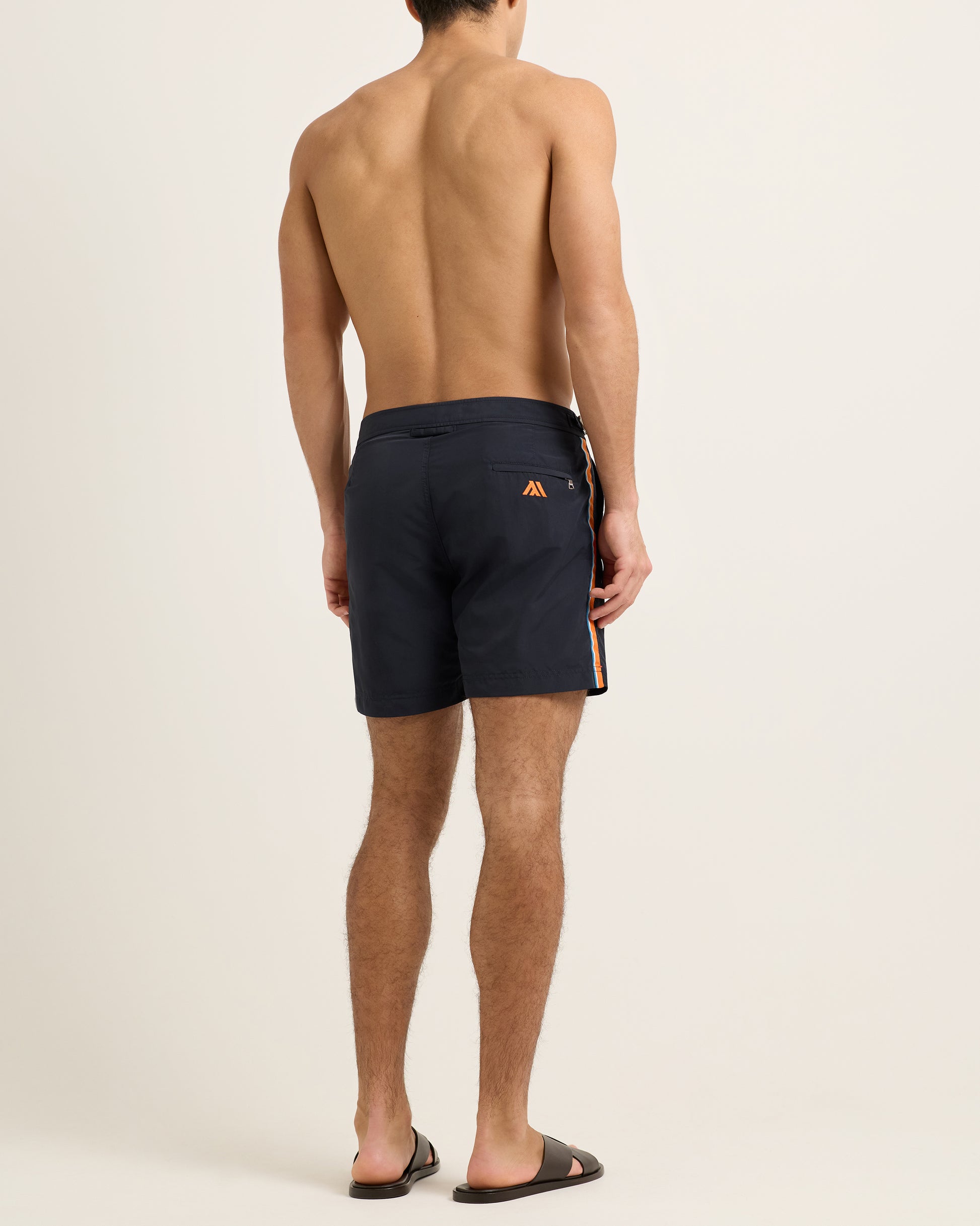 Man wearing black swim shorts with a logo on a beige background