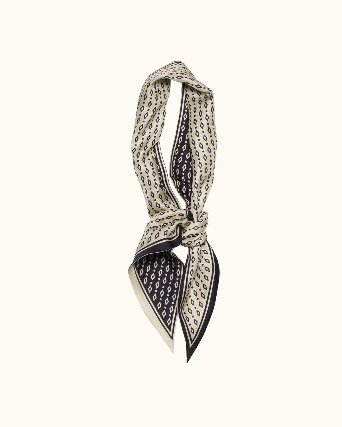 A patterned silk scarf tied in a knot, featuring a black and cream geometric print with a thin black border, set against a plain white background.