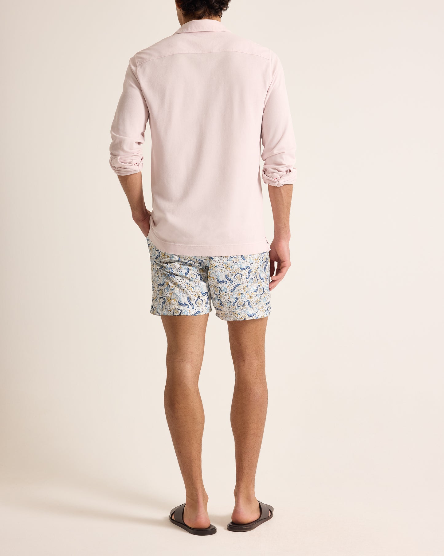 Person wearing a light pink polo shirt and patterned shorts on a plain background