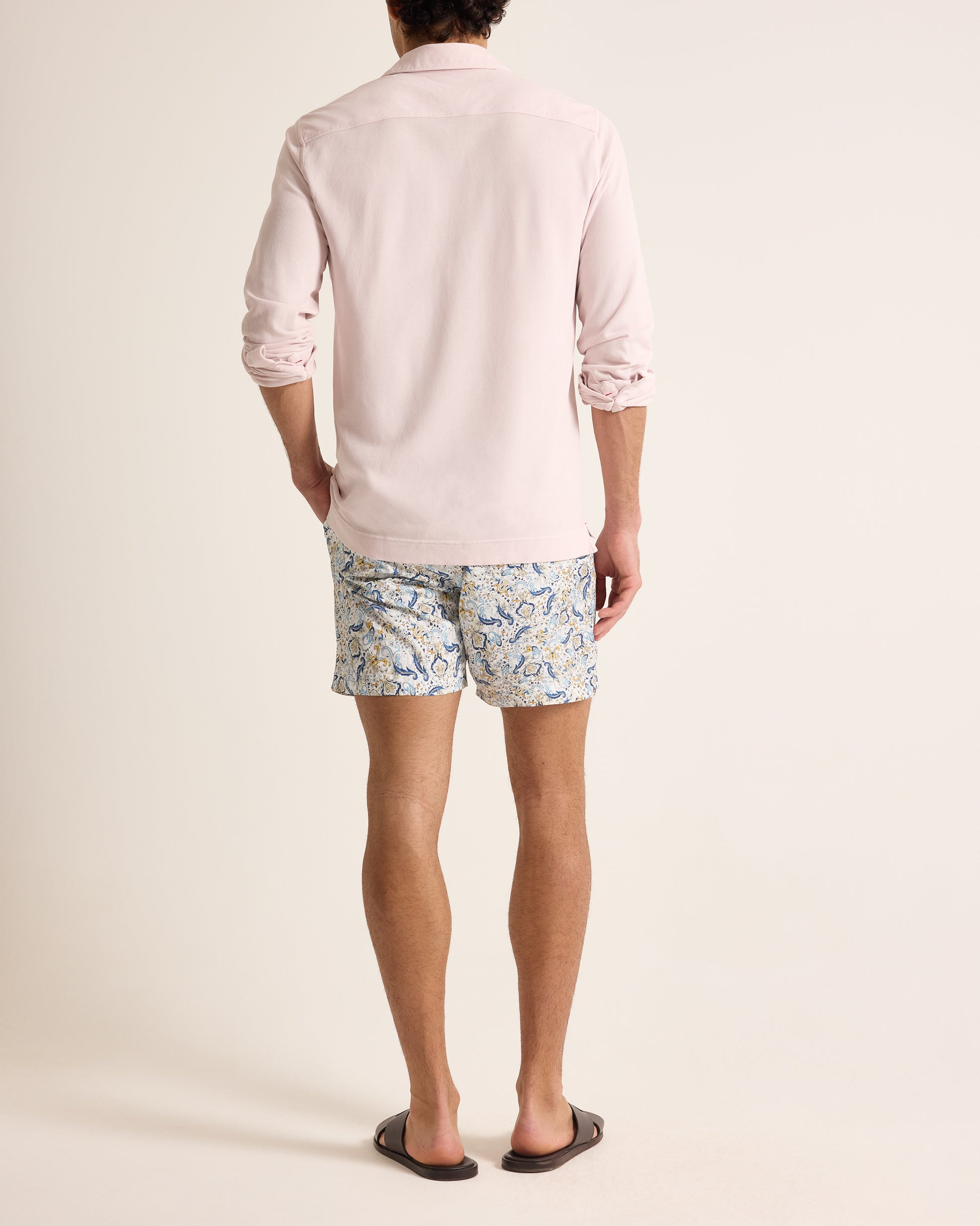 Person wearing a light pink polo shirt and patterned shorts on a plain background