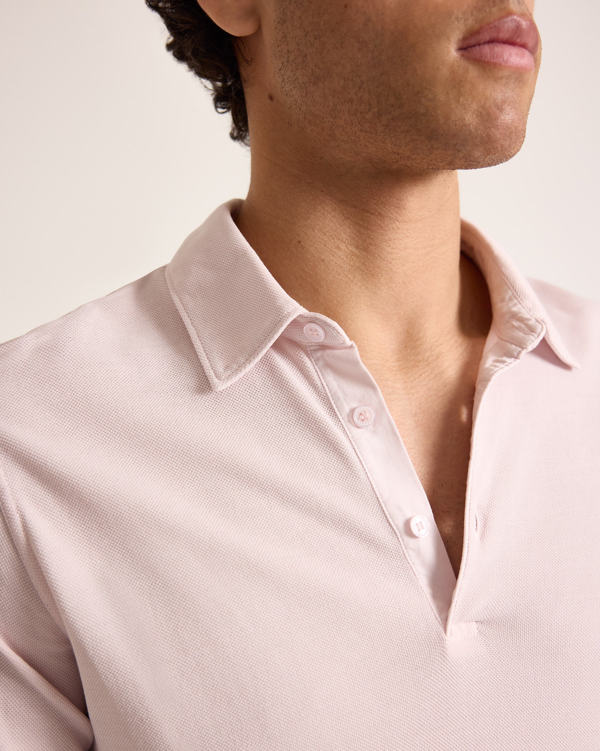 Close-up of a person wearing a light pink polo shirt with a plain background