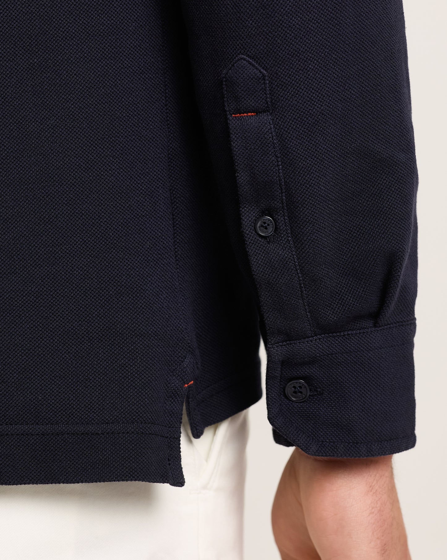 Cuff detail of navy long sleeve polo shirt on a plain background