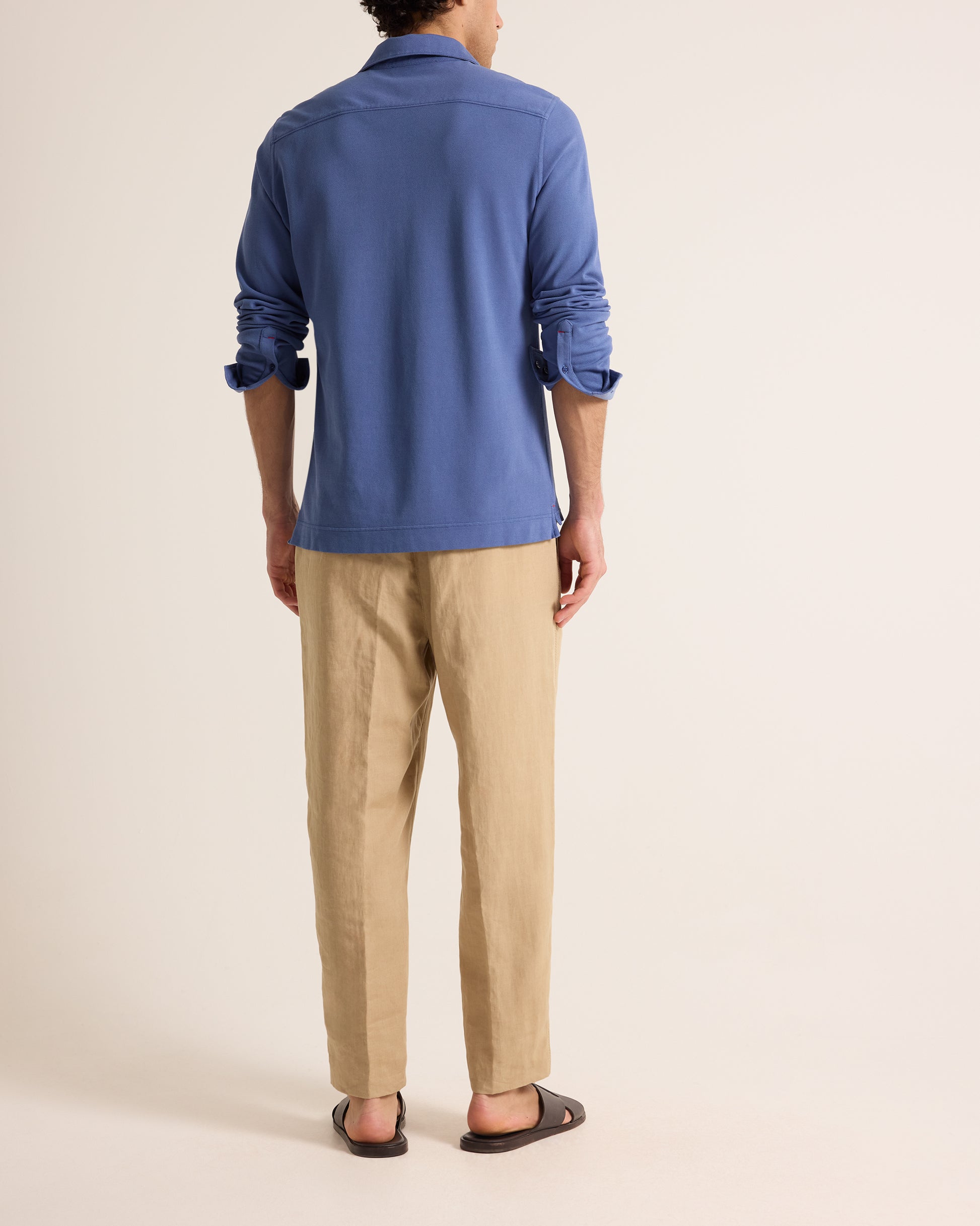 Man wearing blue polo shirt with beige trousers on a plain background