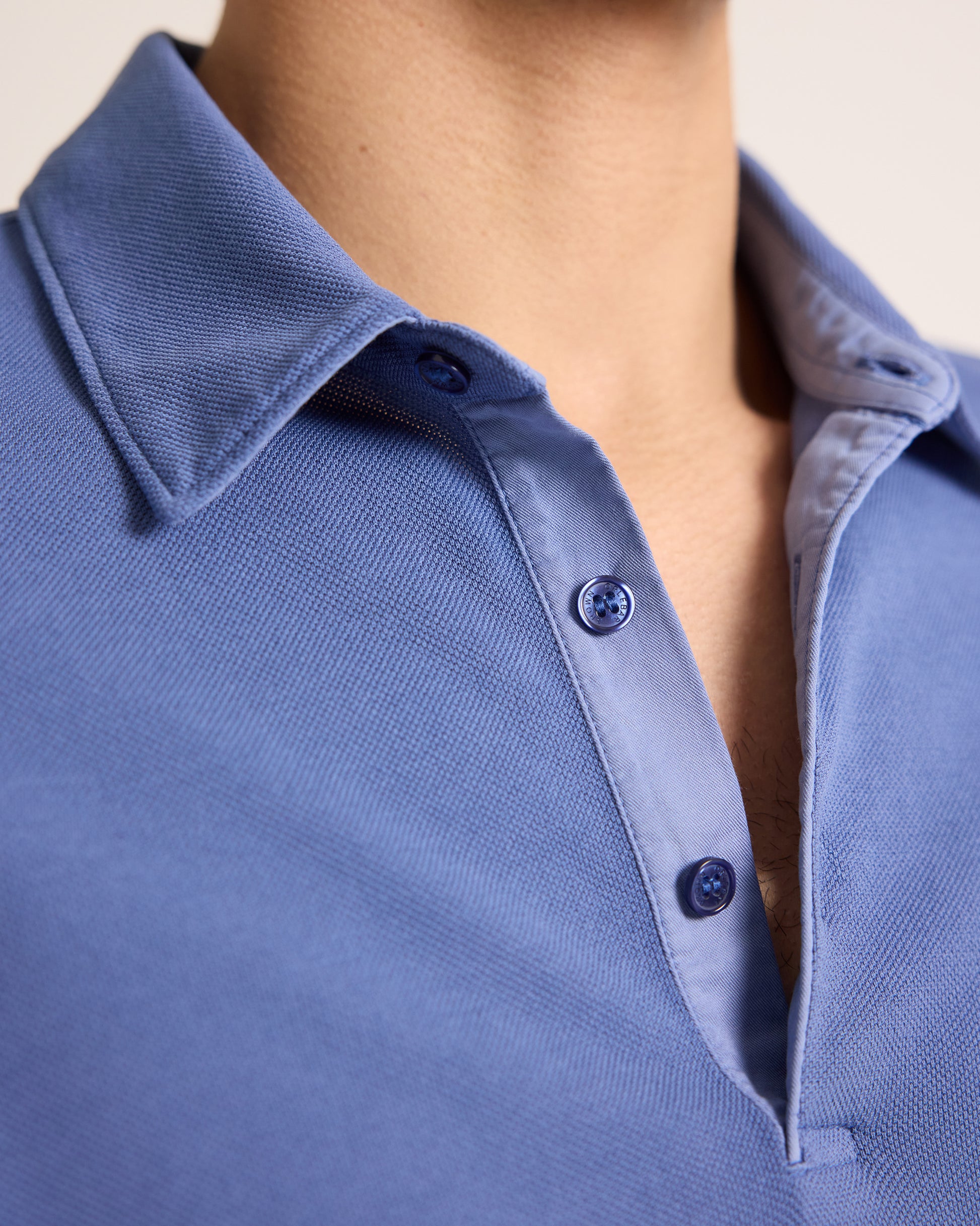 Close-up of a blue polo shirt with buttons on a neutral background