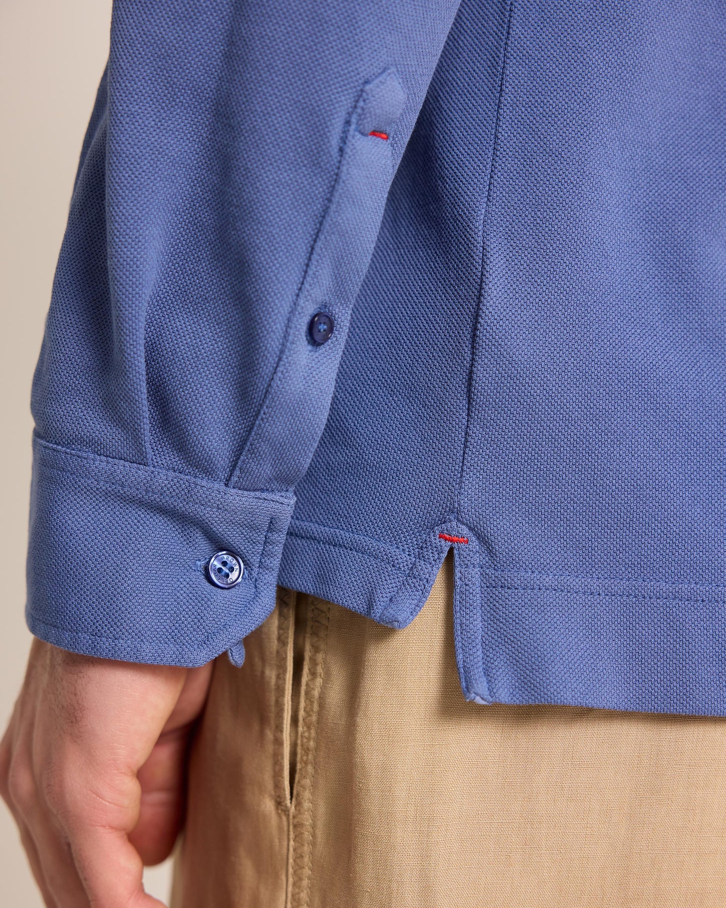 Close-up of a person wearing a blue polo shirt with beige trousers