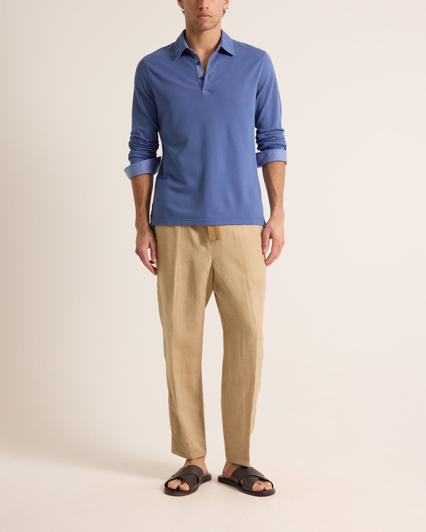 Man wearing blue polo shirt with beige trousers on a plain background