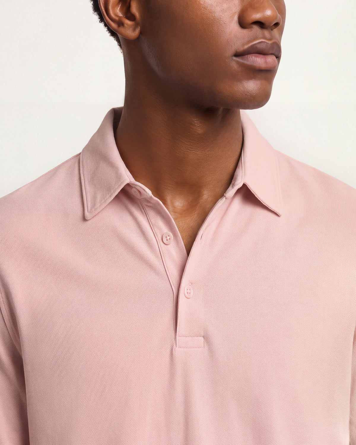 Close-up of a model wearing a light pink polo shirt, showing the collar, button placket, and fabric texture against a plain light background.