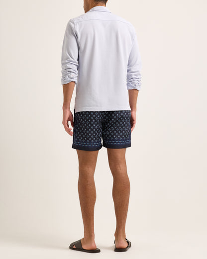 Model wearing light blue long sleeve polo shirt with swim shorts on a plain background