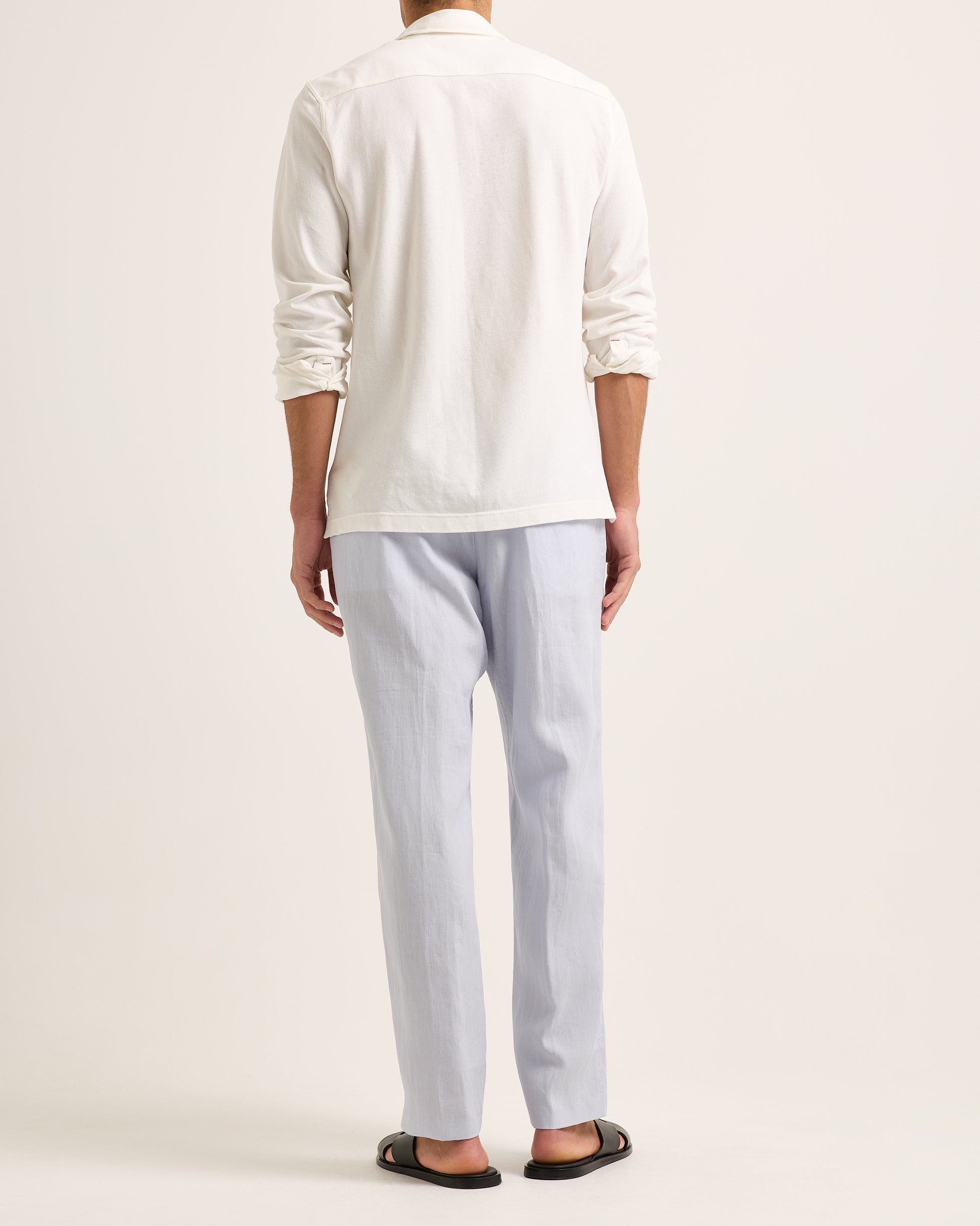 Model wearing white long-sleeve polo shirt with blue trousers on a white background